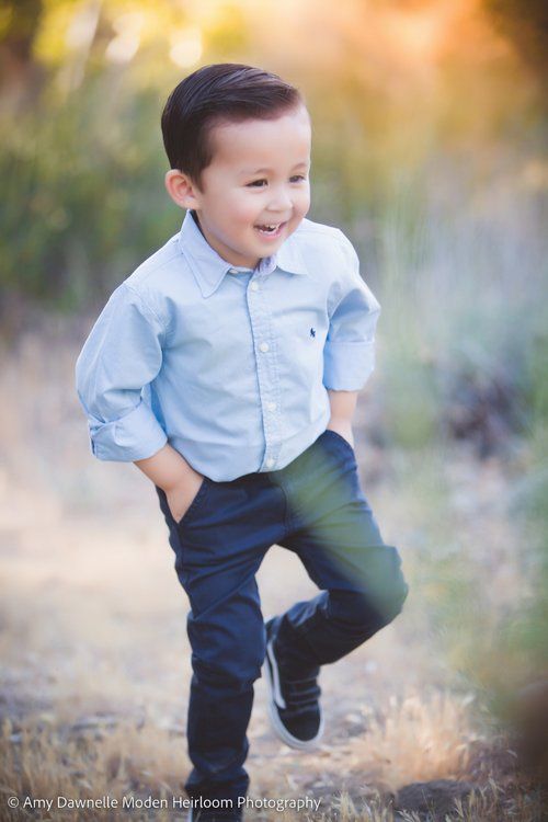 Young child in light blue shirt and navy pants jumping joyfully outdoors at sunset.