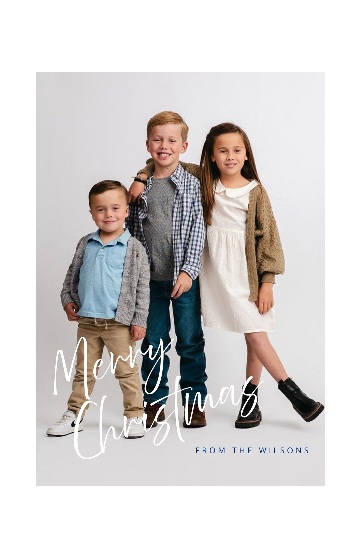 Three children in coordinated casual holiday outfits pose together against a light gray background for a Christmas card photo.