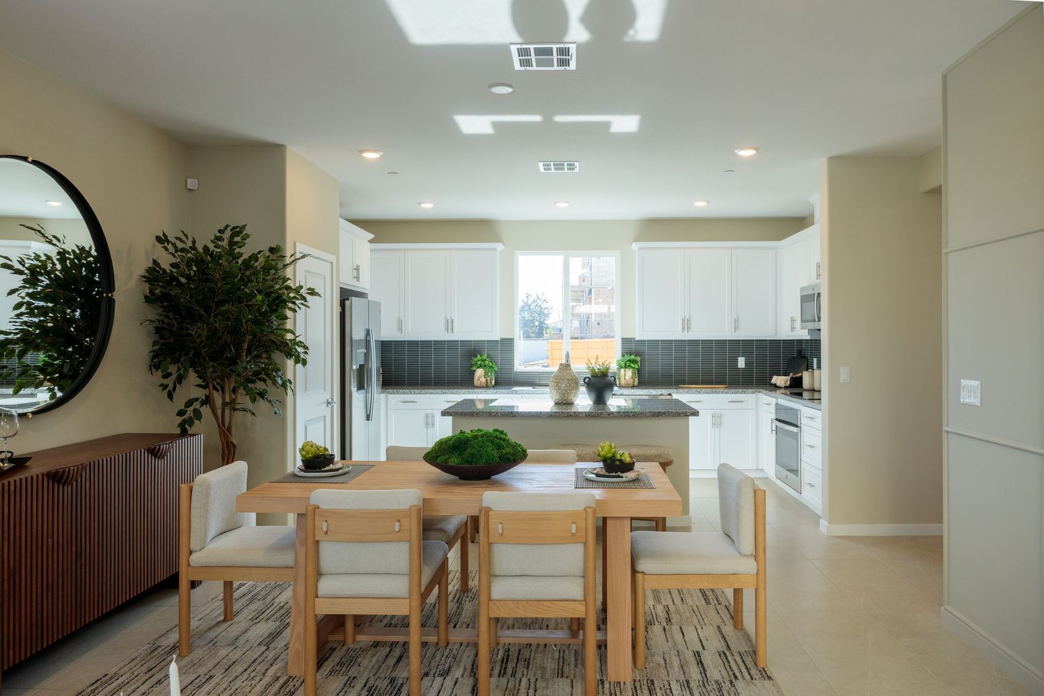 Modern open concept apartment interior with wooden dining table and natural light streaming through large windows.