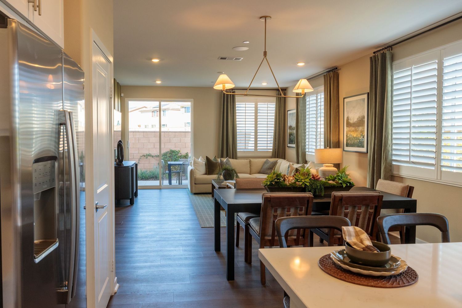Modern open concept kitchen and living area with dark hardwood floors, white cabinets, and plantation shutters.