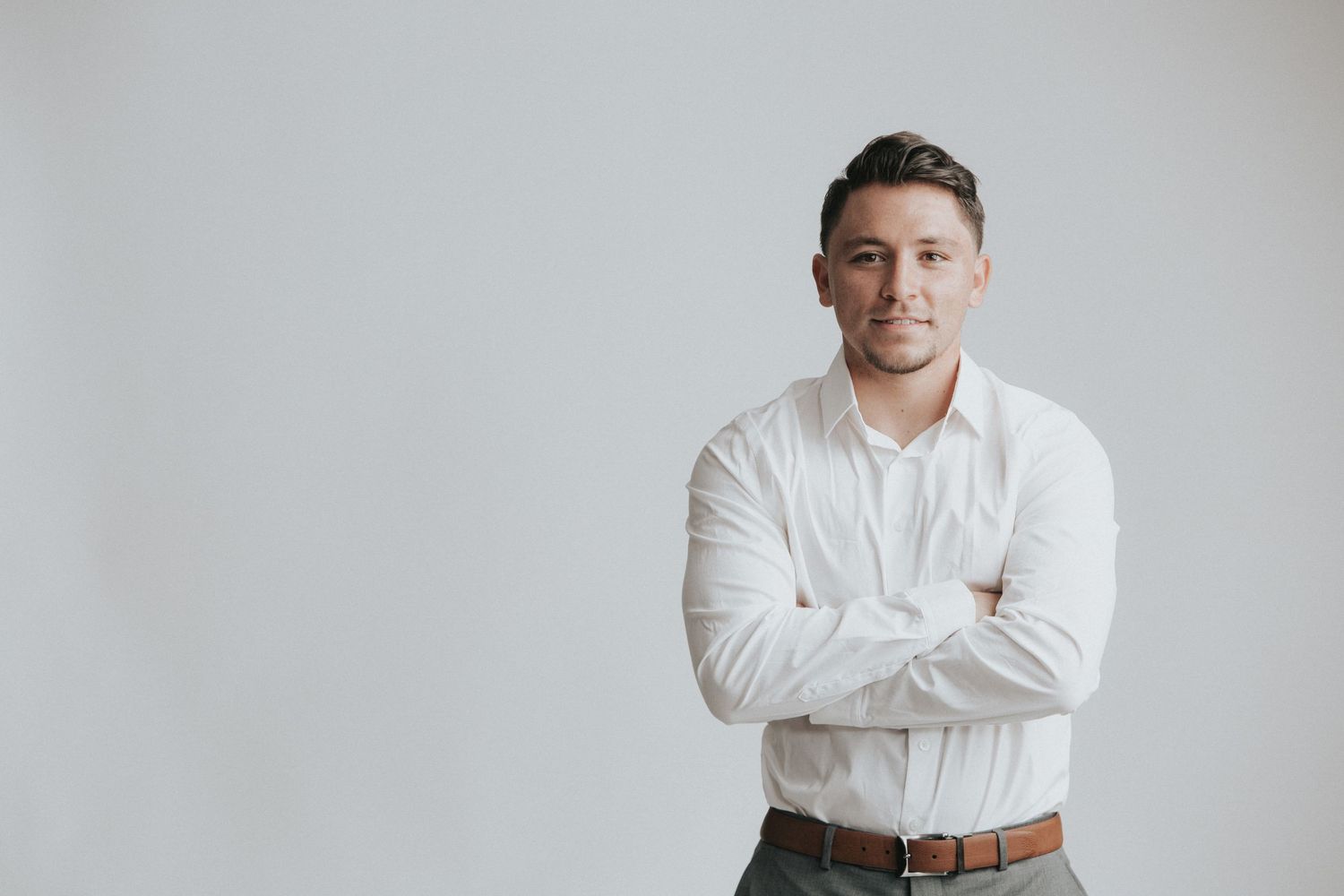 Professional portrait of someone in a crisp white button down shirt with arms crossed against a light gray background.