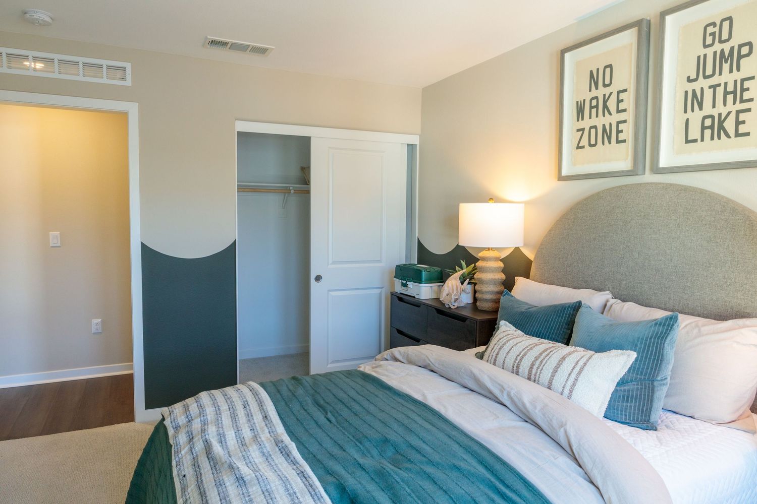 Modern bedroom interior with coastal decor featuring blue bedding, white walls, and framed artwork above the bed.