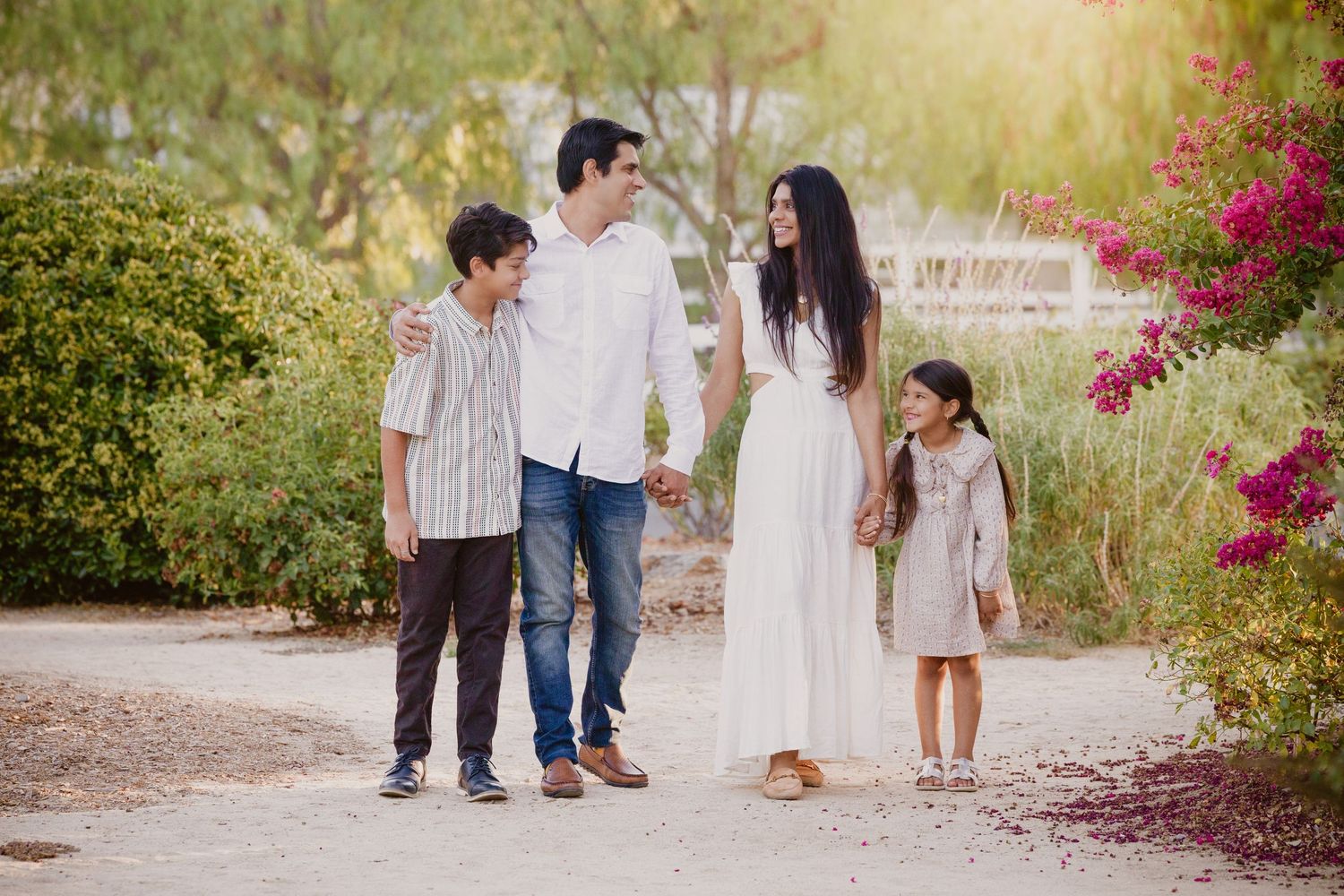 Family members stroll together on a scenic path with blooming bougainvillea flowers in the background.