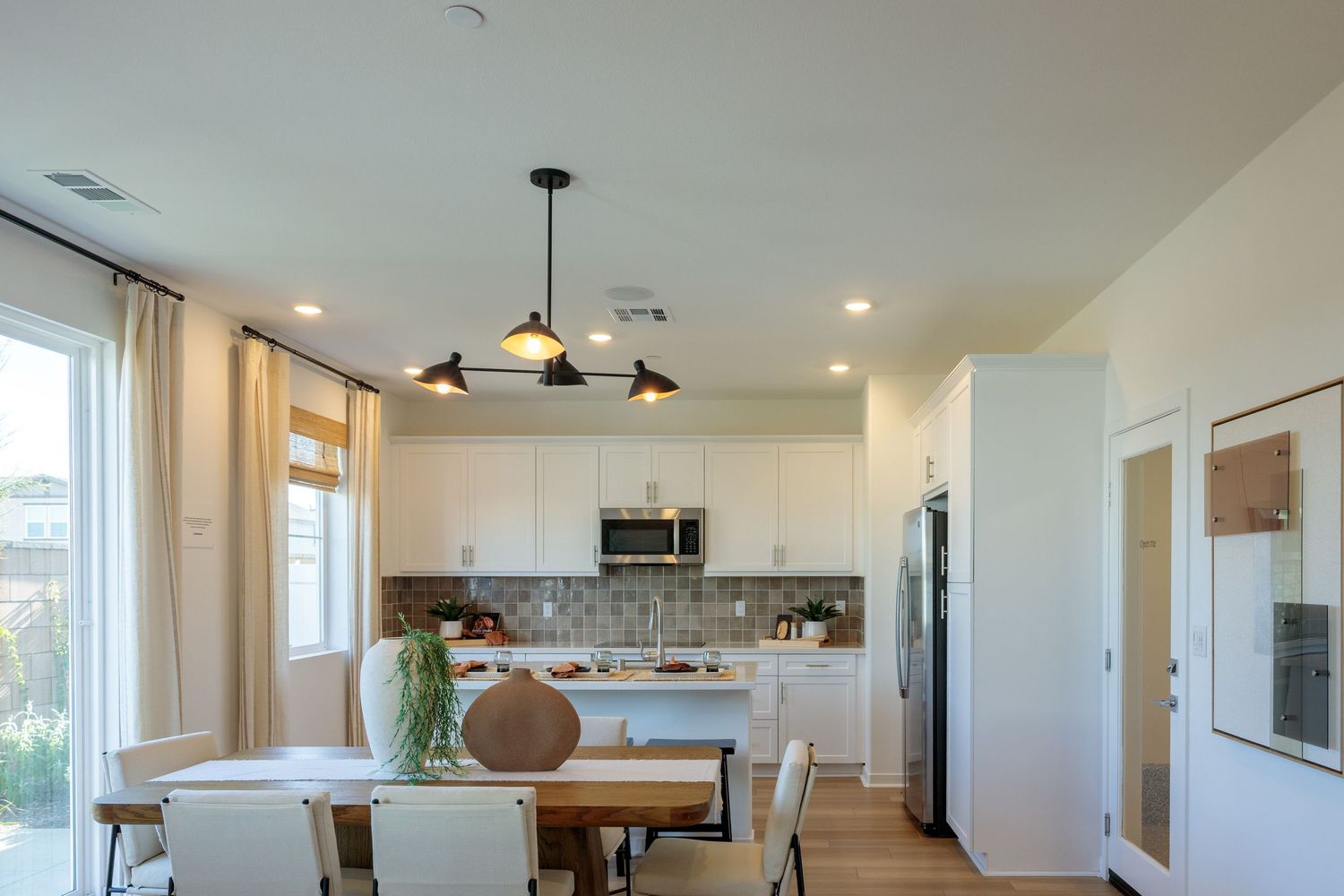 Modern open concept kitchen and living area with white cabinets, pendant lights, and large windows letting in natural light.