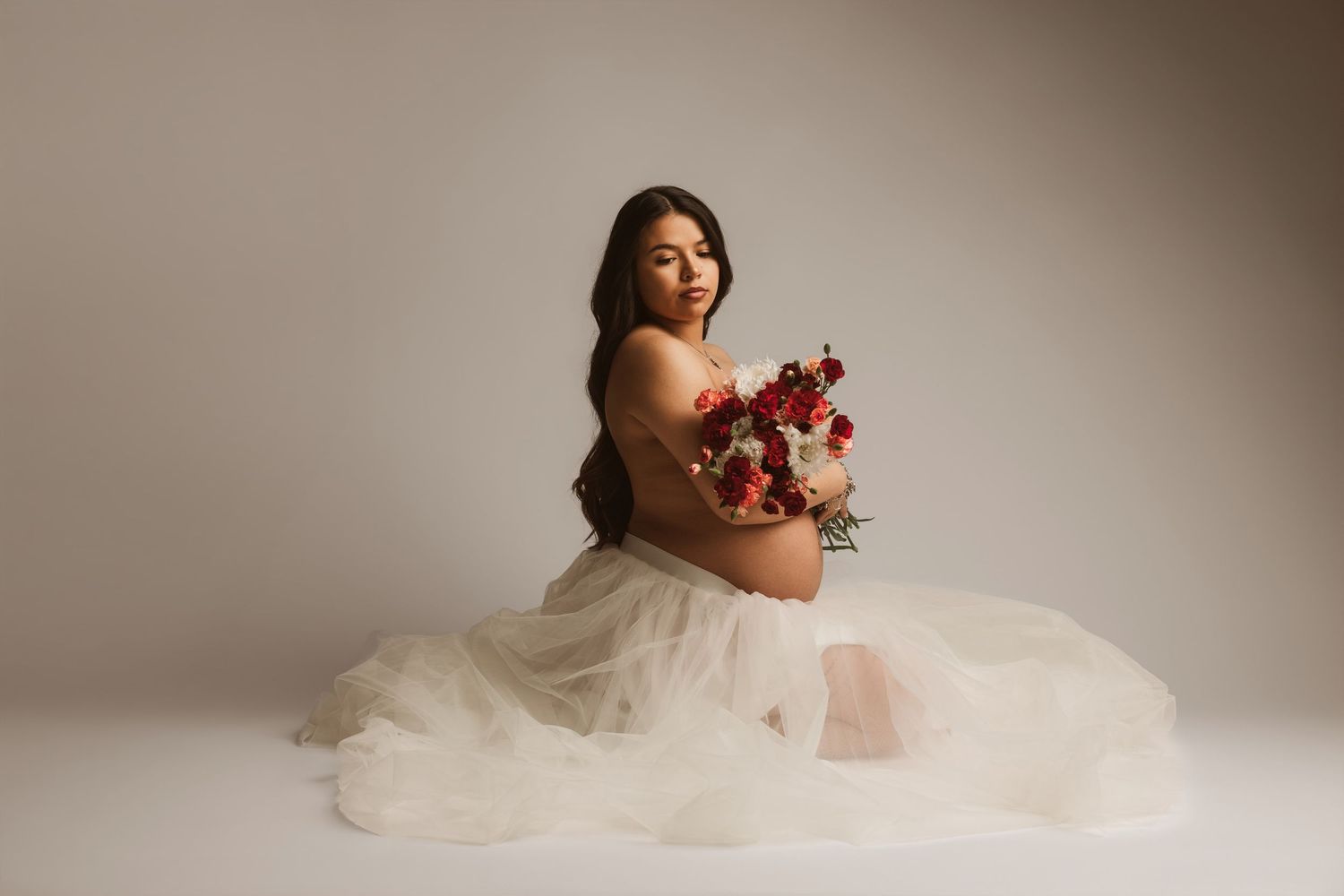 A person in a flowing white wedding dress poses gracefully against a neutral studio backdrop.