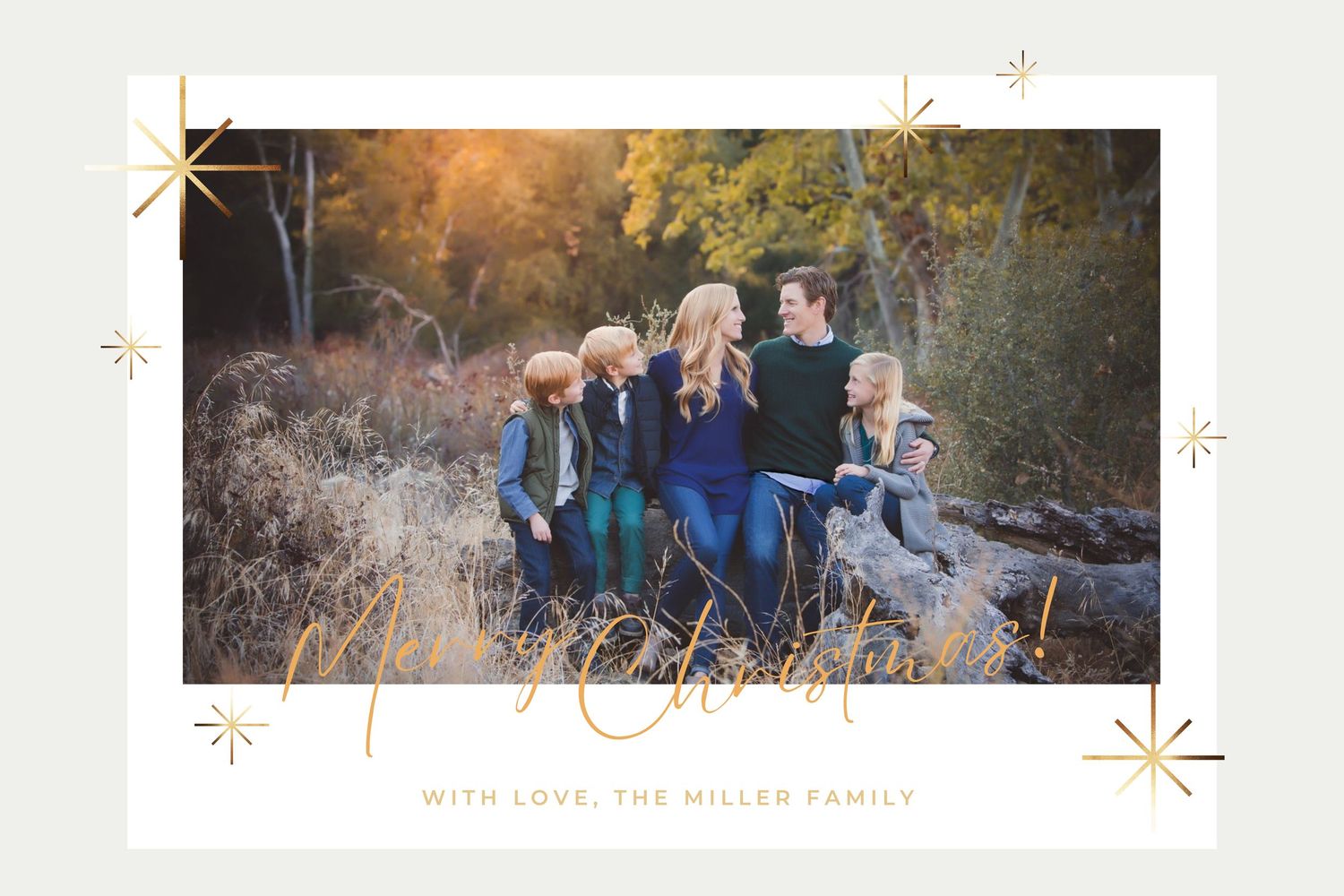 A family sits together outdoors in a natural setting at sunset with decorative gold stars framing the photograph.