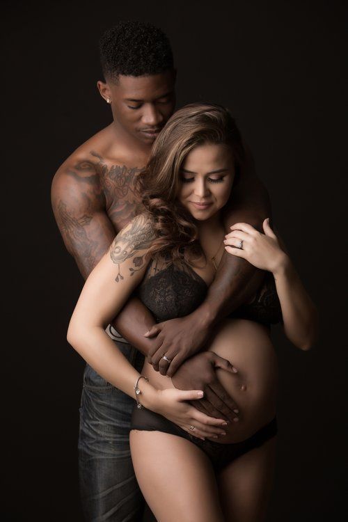 A romantic maternity photo series featuring an intimate couple in dark lighting against a black background.