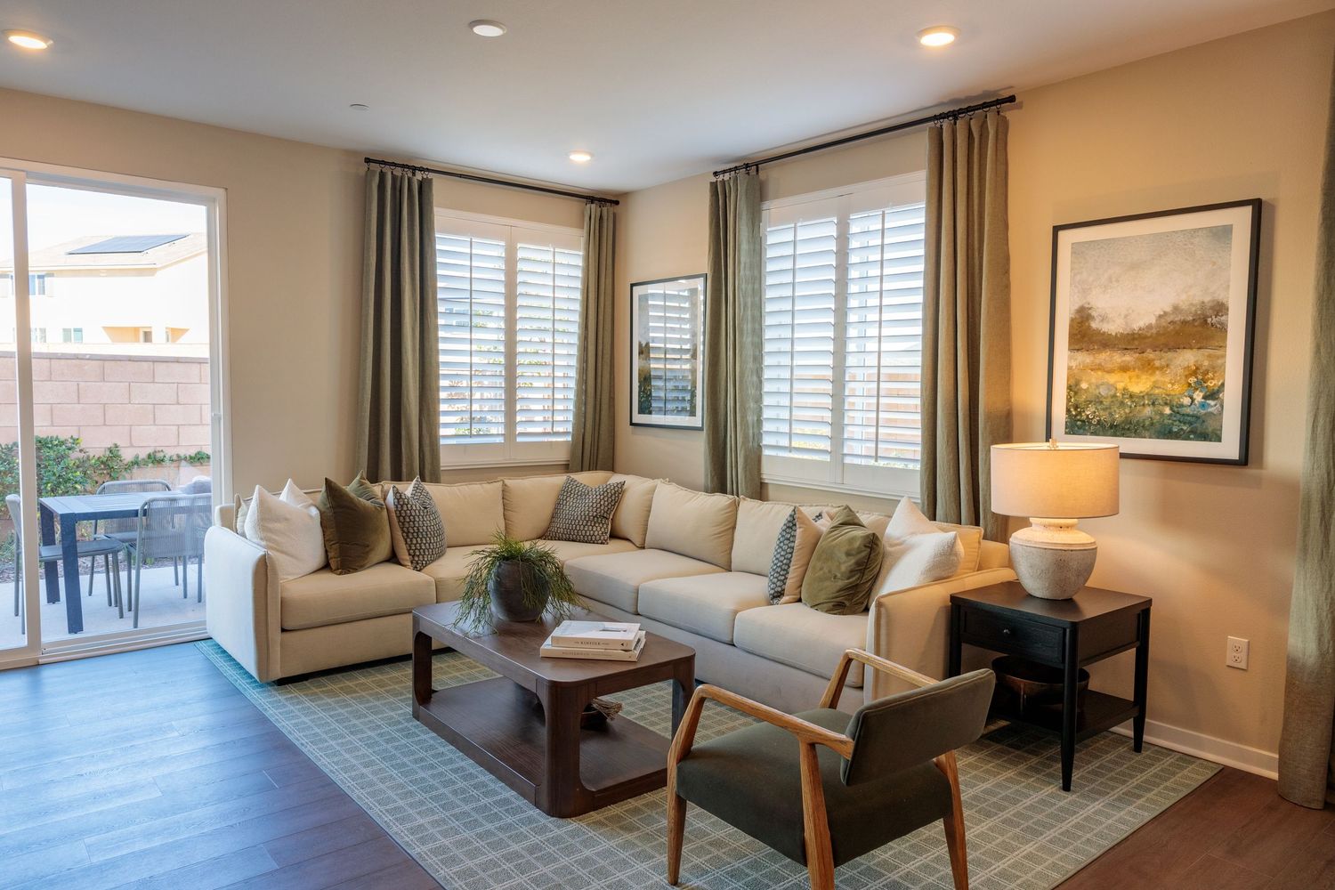 Modern living room interior with recessed lighting, beige walls, and large windows featuring contemporary furnishings.