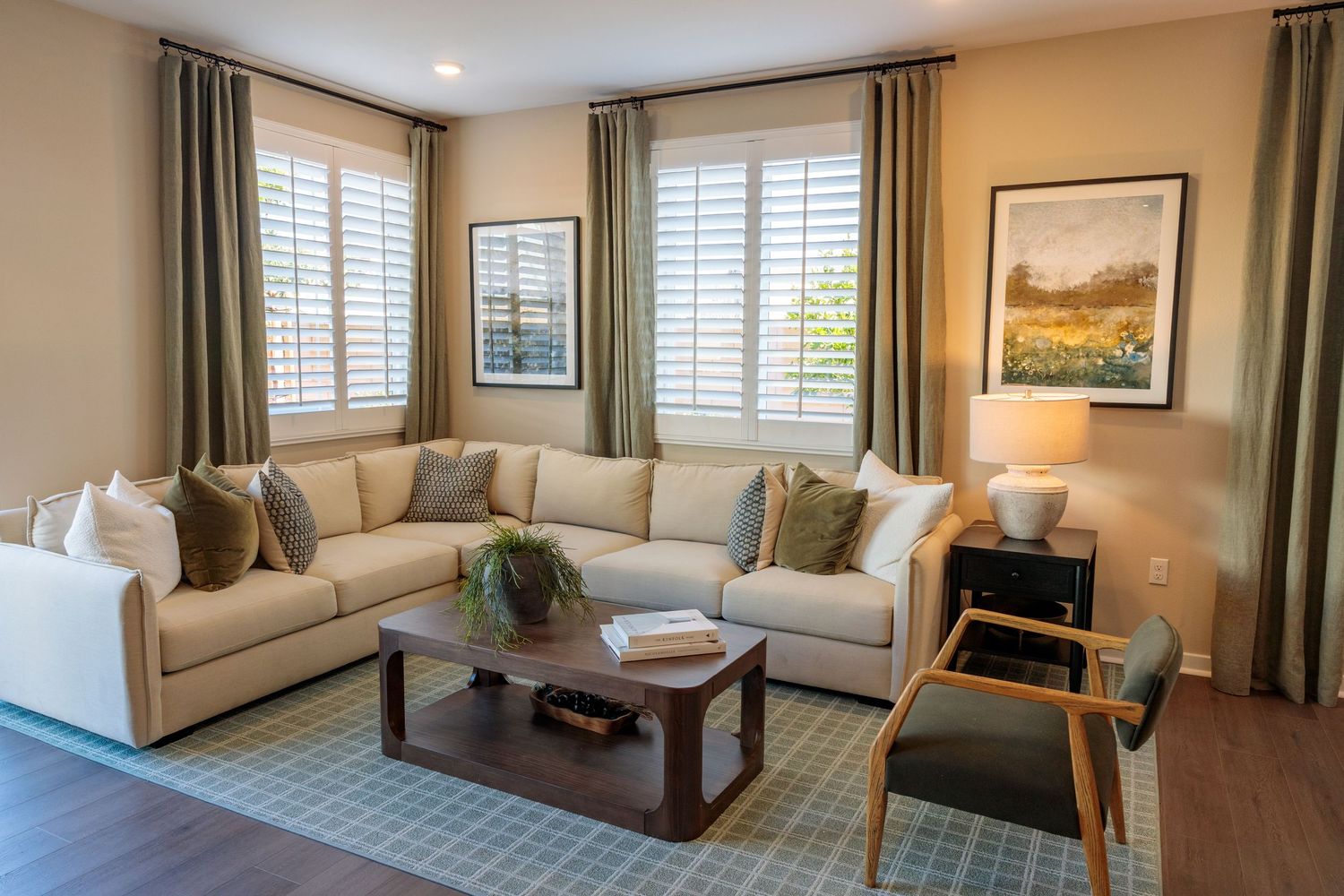 Panoramic view of a modern living room with beige walls, white shutters, and elegant curtains showing multiple seating areas.