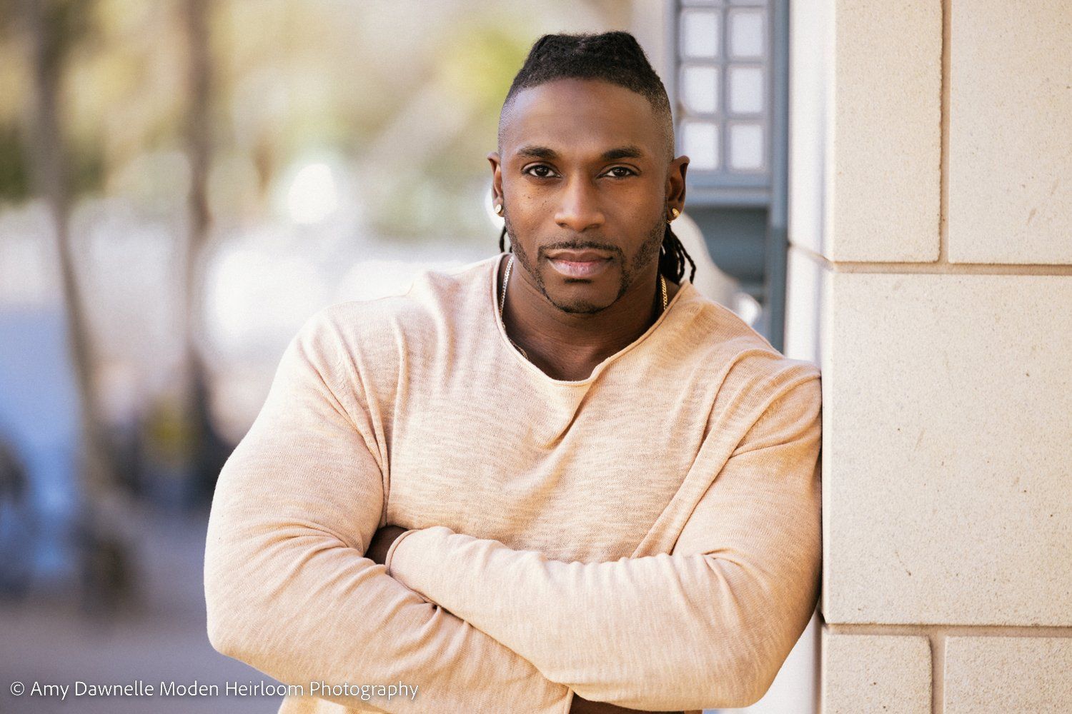 A person wearing a light peach colored sweater poses against a neutral wall with a soft smile.