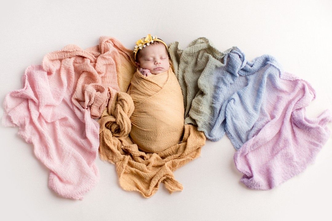 Colorful baby onesies and bodysuits arranged in a neat row on a white surface.