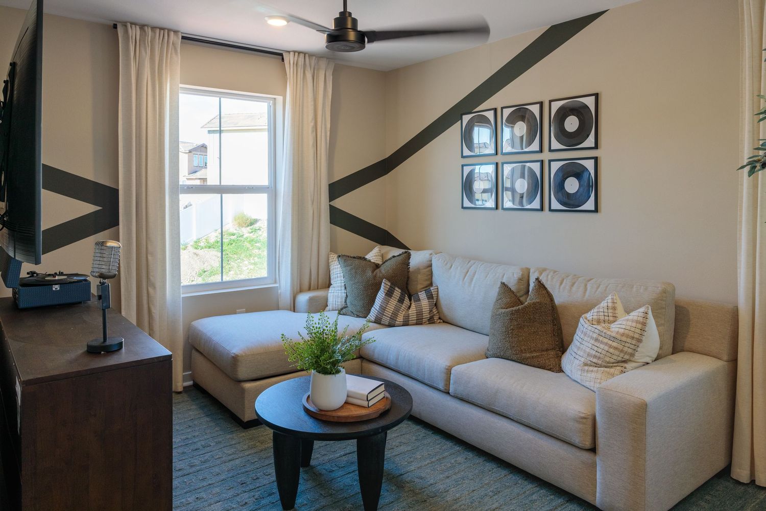 Modern living room with gray sectional sofa, round coffee table, and framed artwork displayed on beige walls.