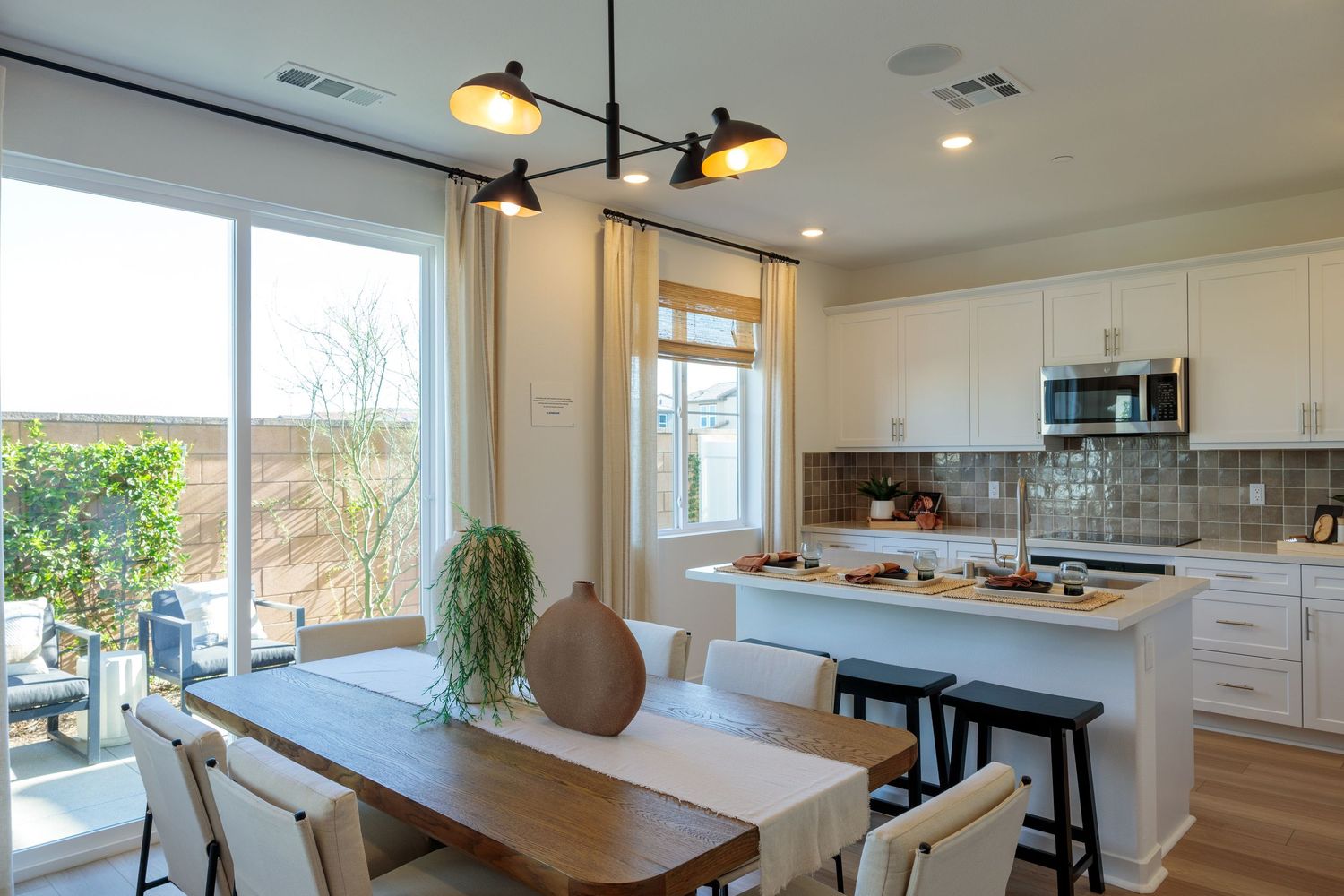Modern open concept kitchen and dining area with white cabinets, wood floors and large windows overlooking outdoor greenery.