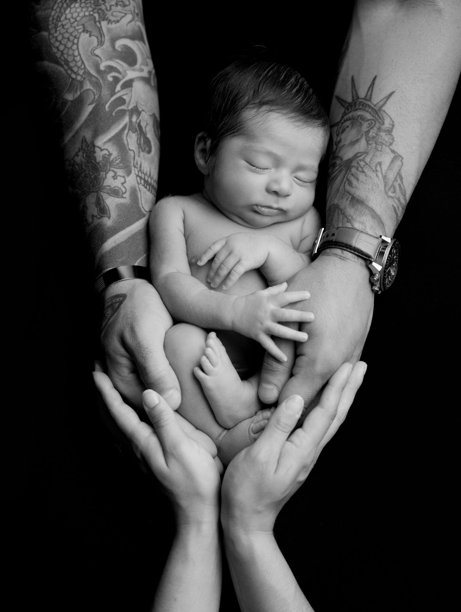 A series of black and white photographs show gentle hands cradling a sleeping newborn baby against a dark background.