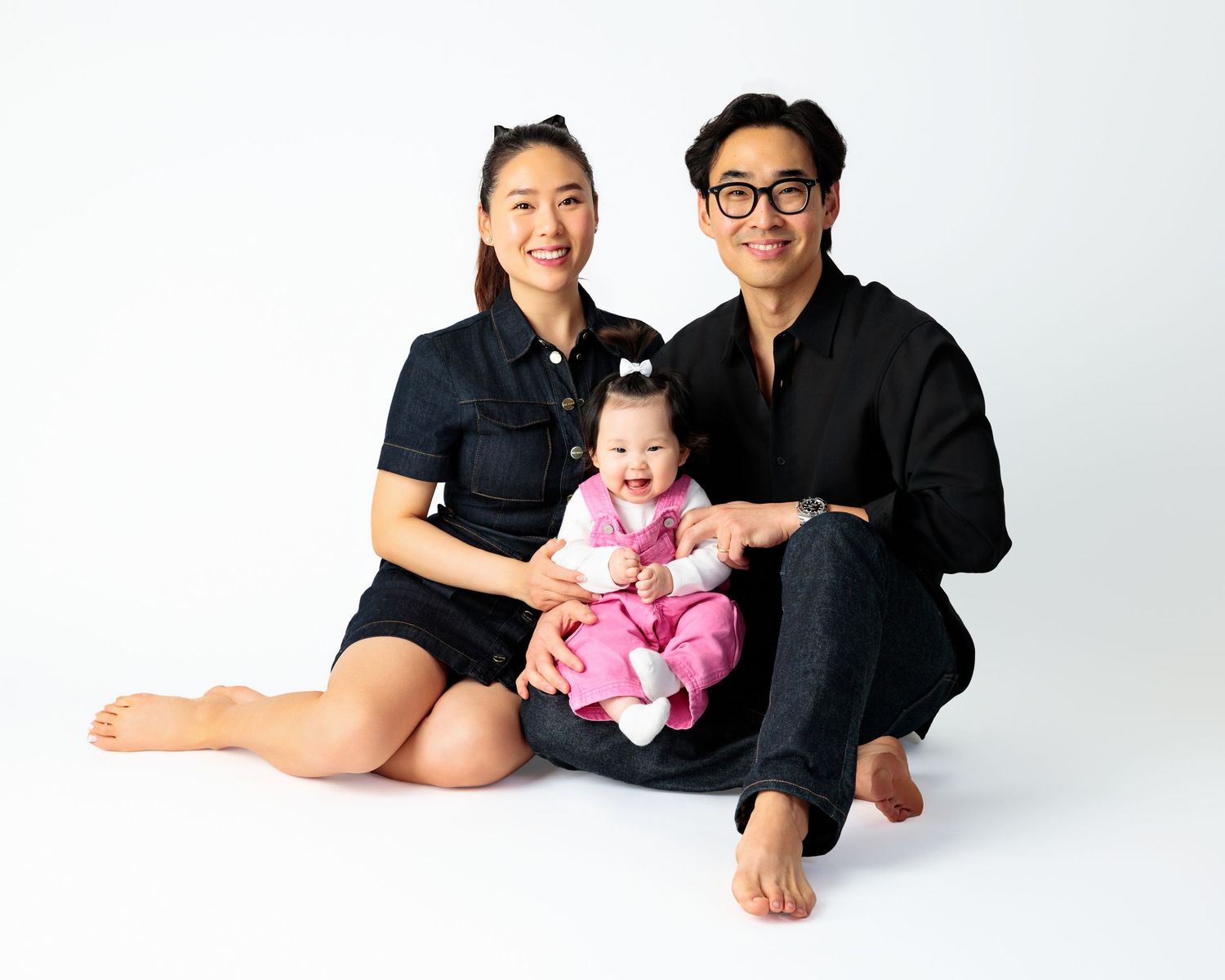 Family of three wearing black outfits poses together in studio against white backdrop in three different poses.