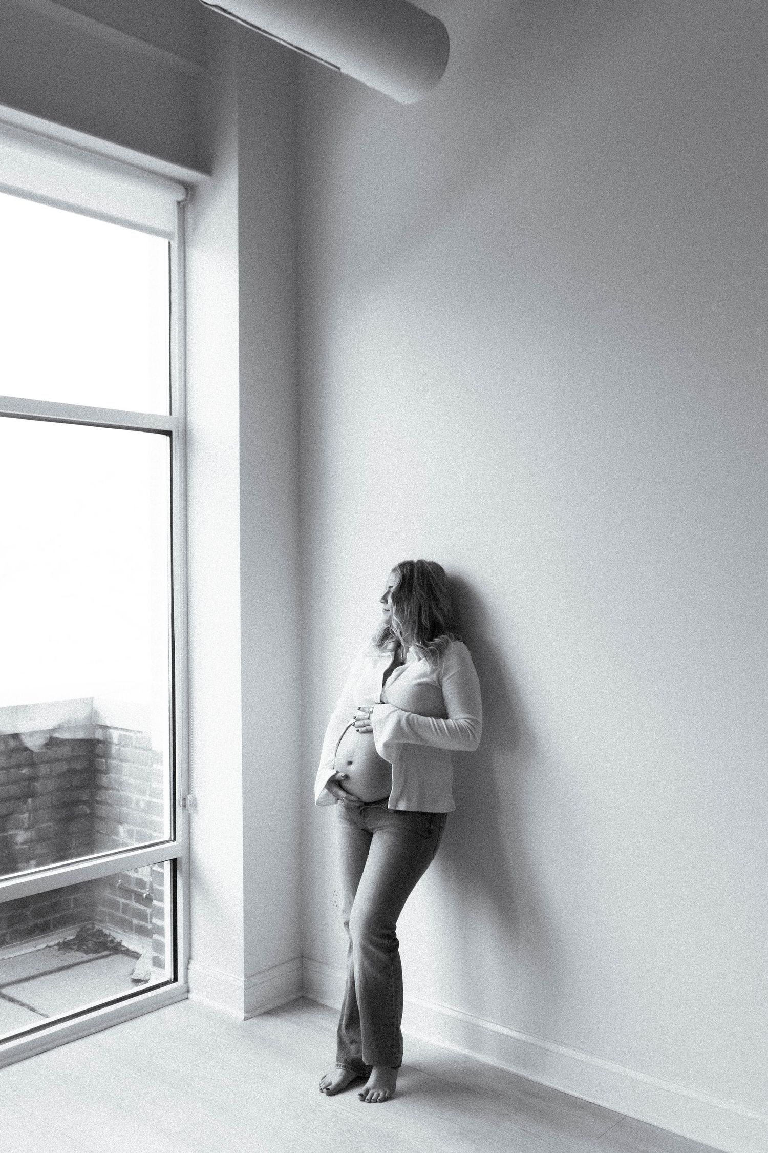 A black and white photo series showing a person in white crouched by a window in an empty minimalist room.
