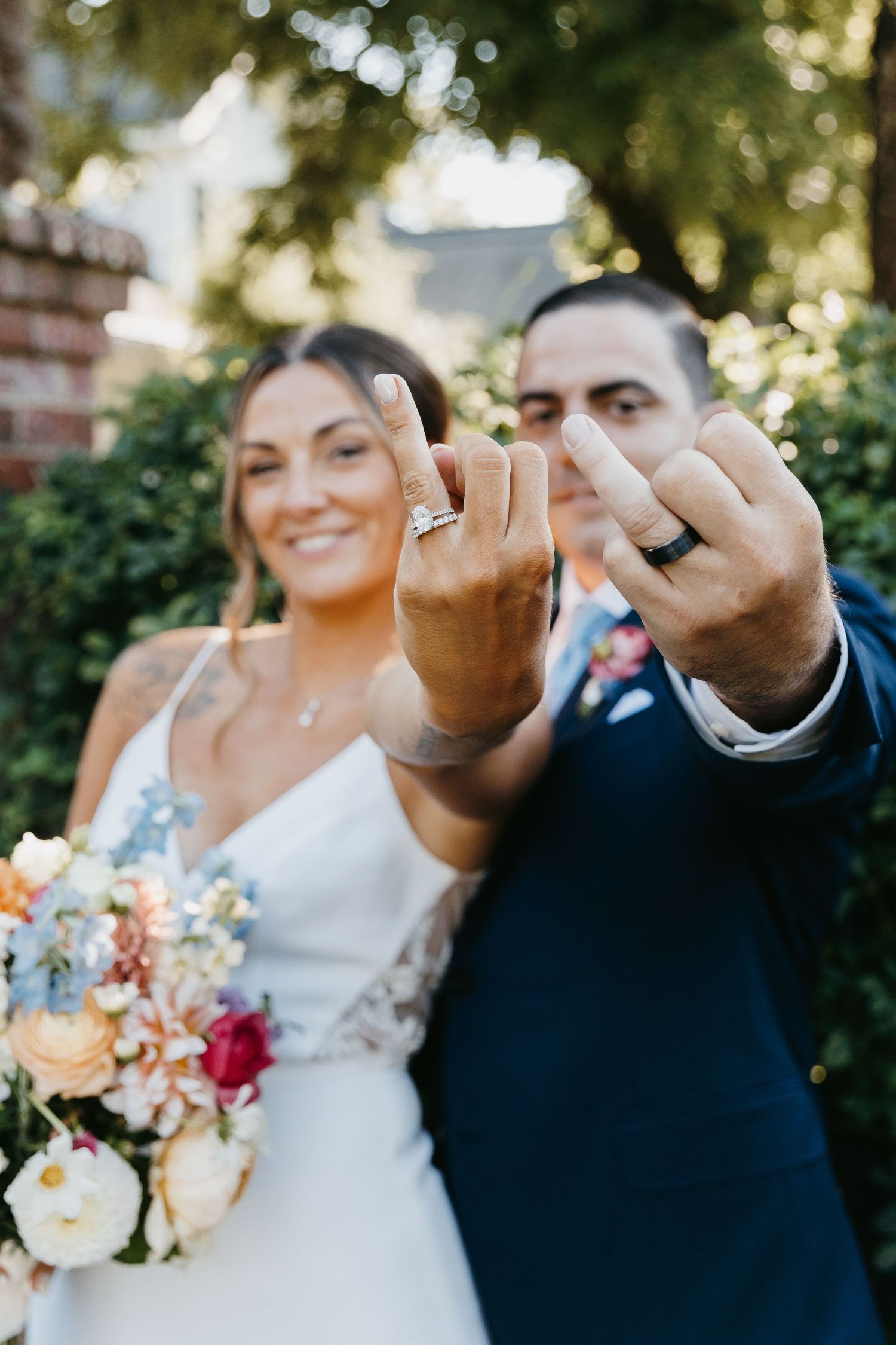 Newlyweds showing off their wedding rings with colorful bouquet in background.