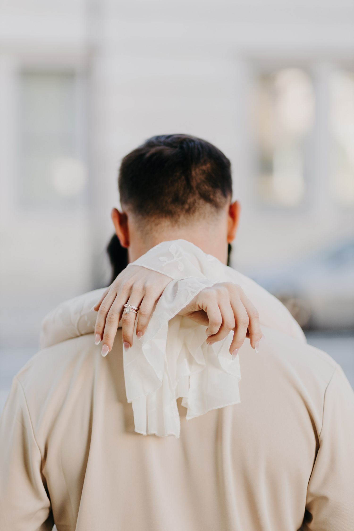 Back view of person in beige coat with hands showing wedding ring.