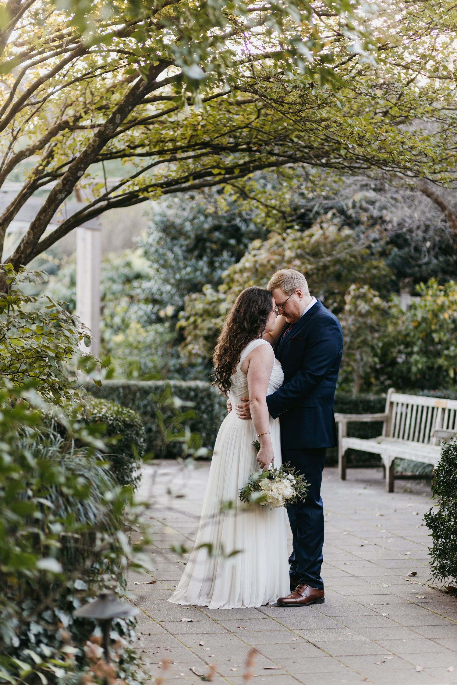 Romantic garden wedding scene with couple standing on stone path under flowering trees.