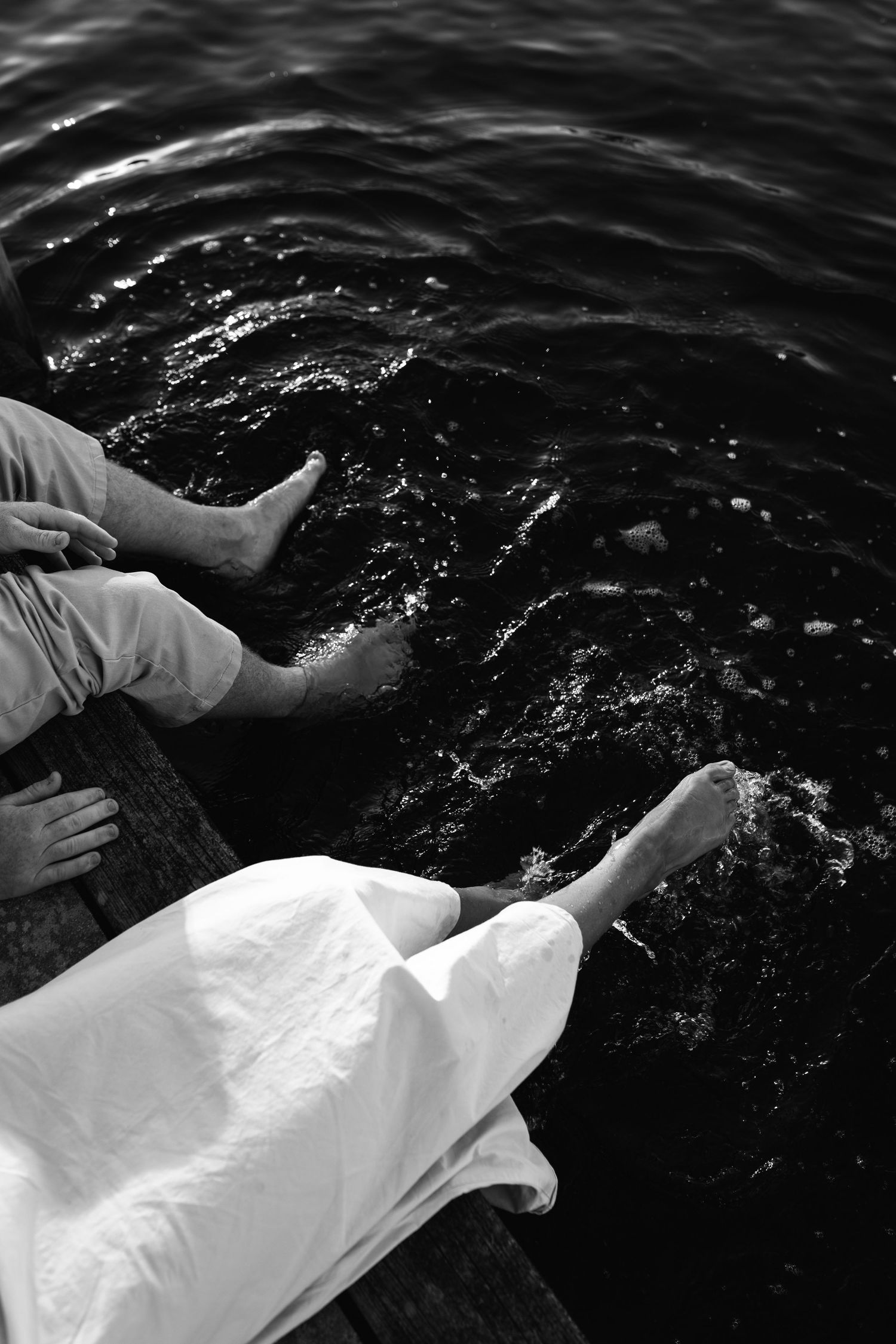 A sequence of black and white photos showing hands reaching into dark rippling water while wearing white fabric.