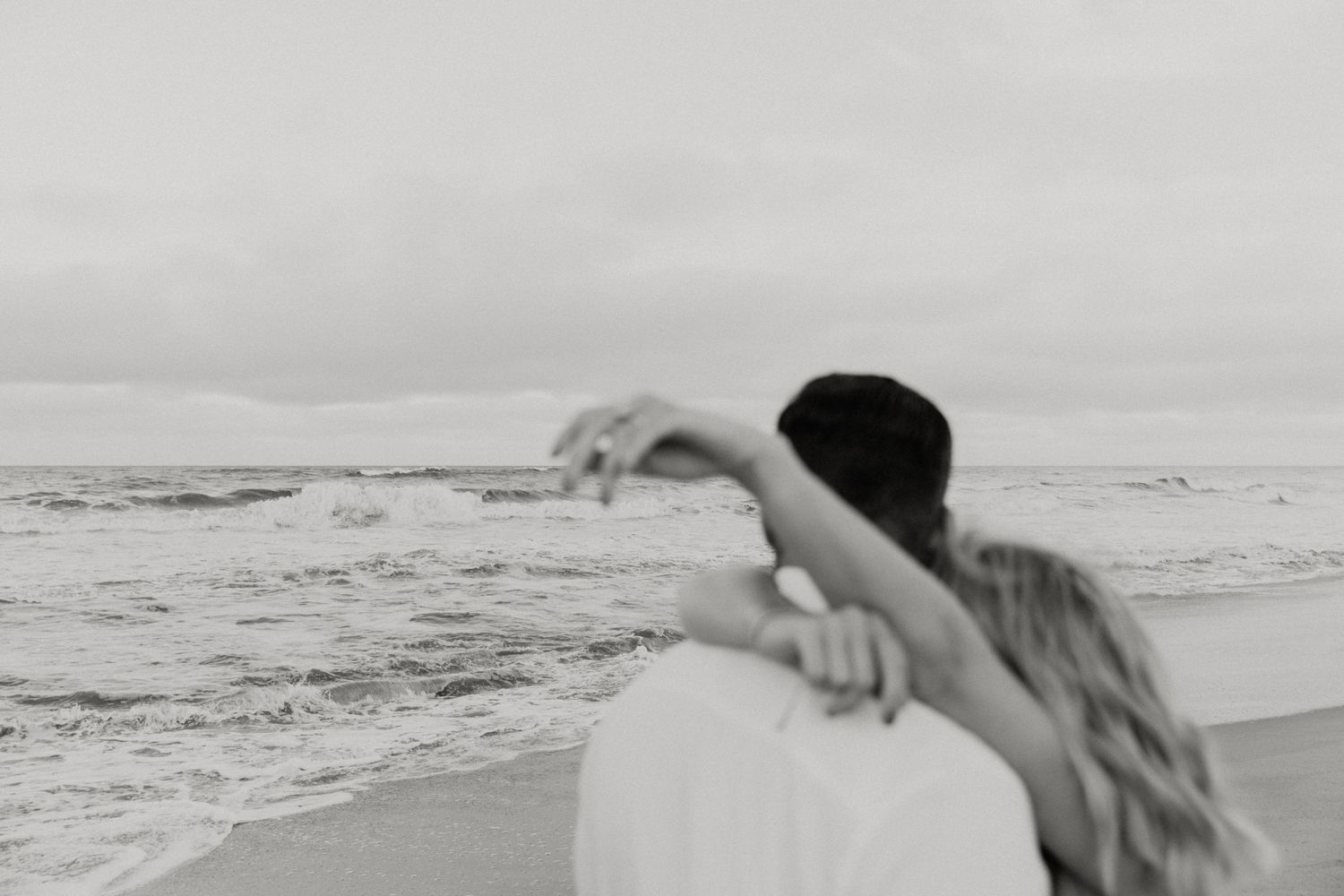 Black and white romantic beach scene with couple embracing by the ocean.