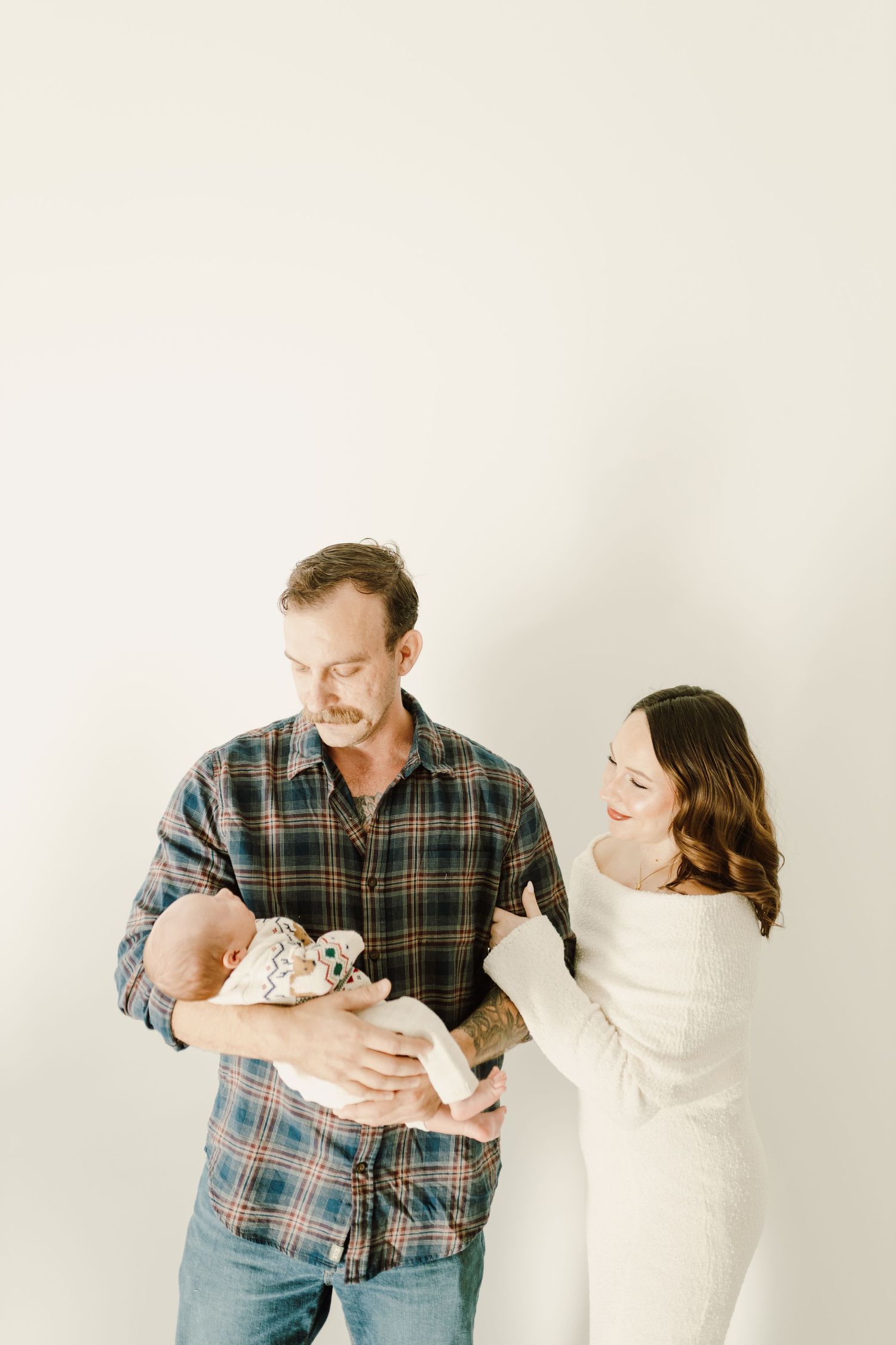 Family portrait against white background with parents holding newborn baby.