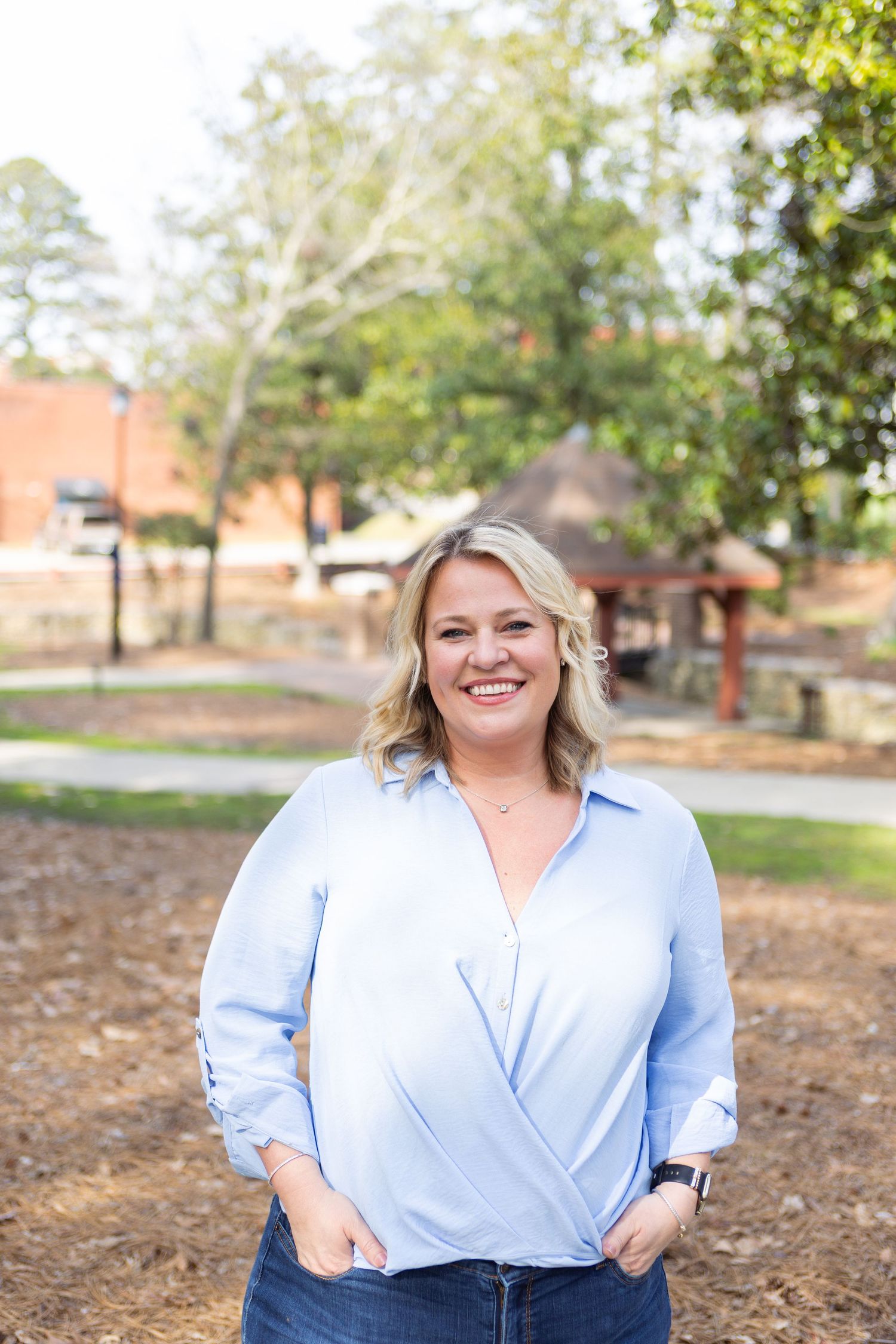 Casual outdoor portrait featuring a light blue wrap top and jeans against a natural background.