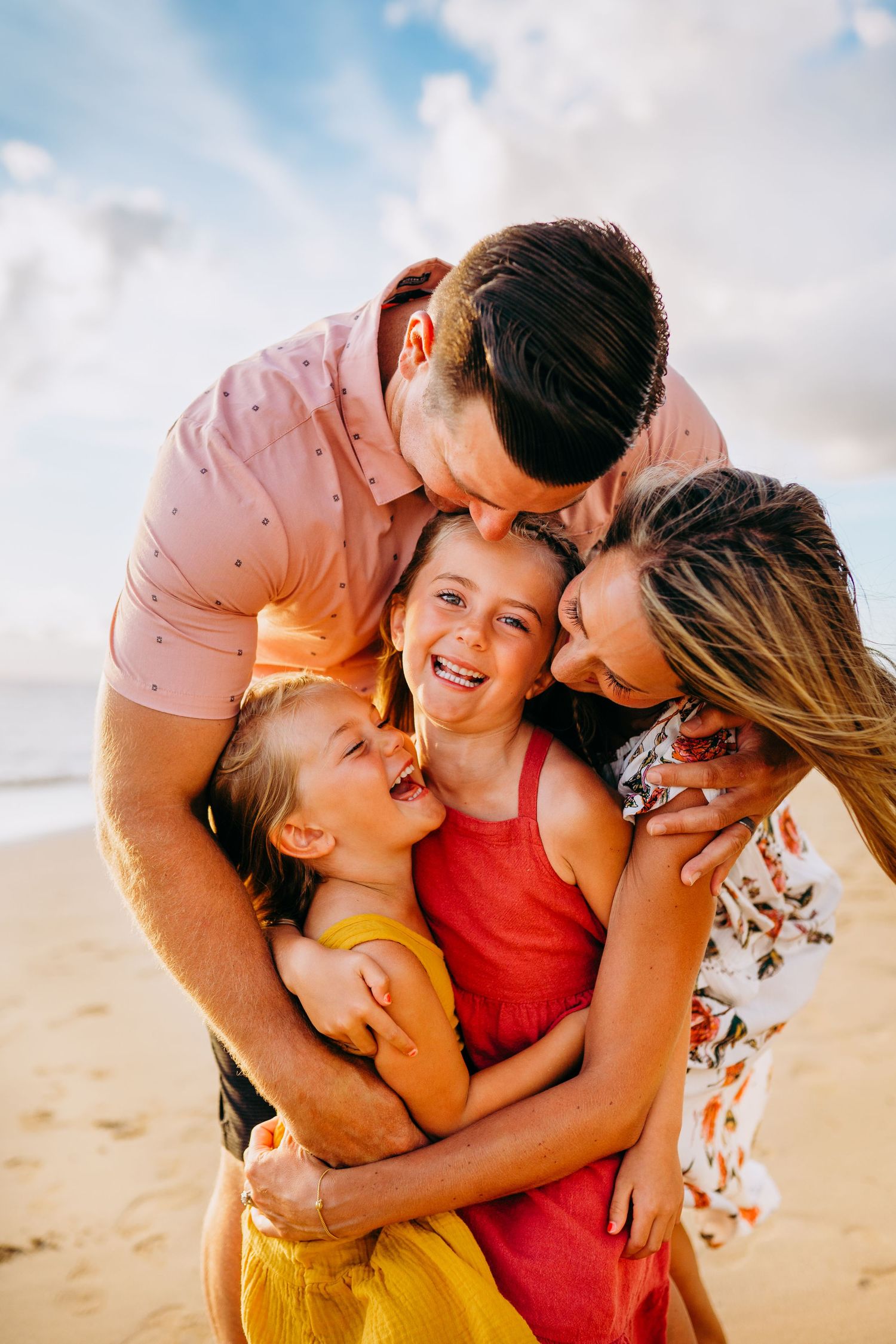 A loving family shares joyful laughter and embraces together on a sunny beach at sunset.