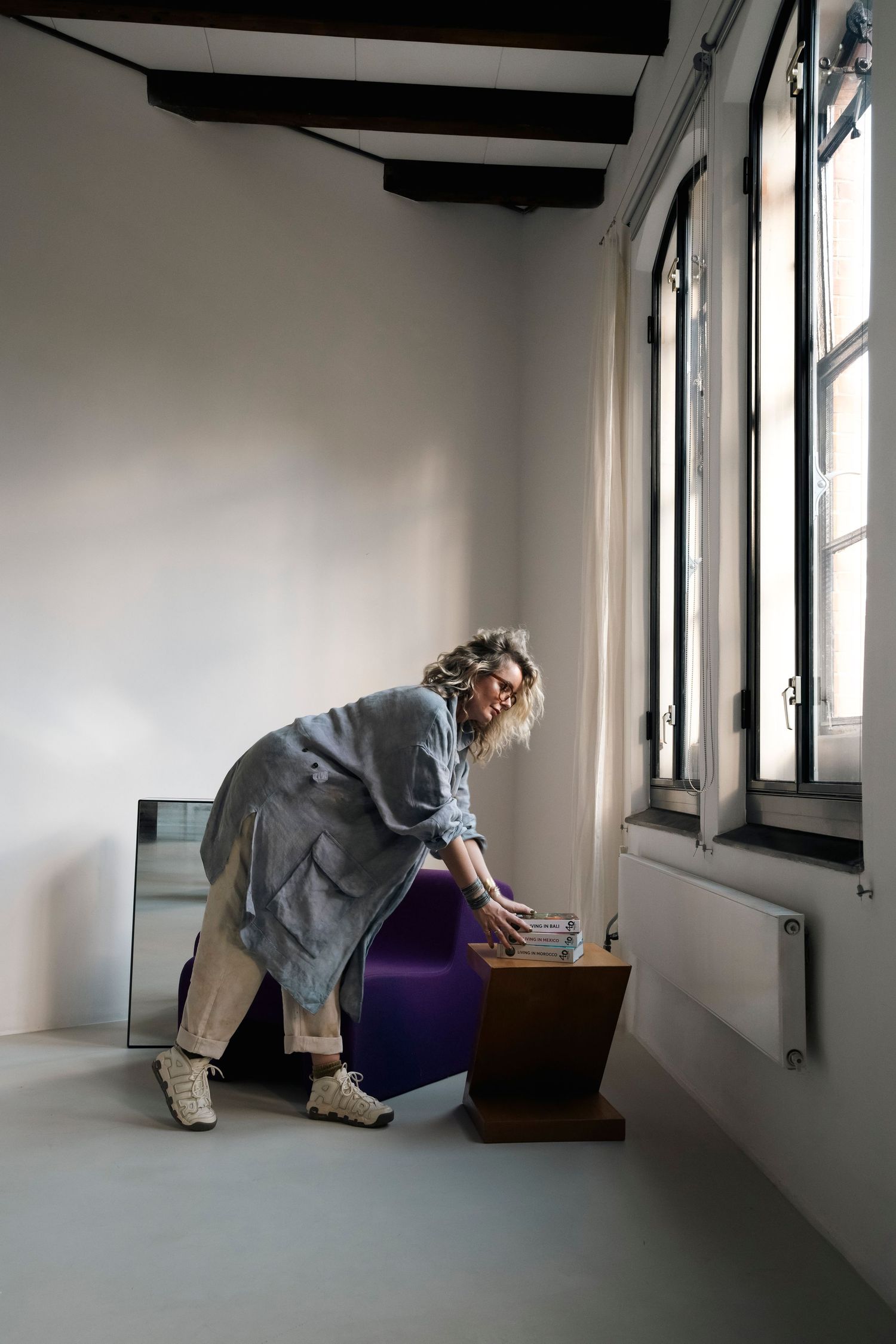 Vrouwelijke styliste richt een ruimte in, plaatst accessoires op een tafel, stapel boeken.