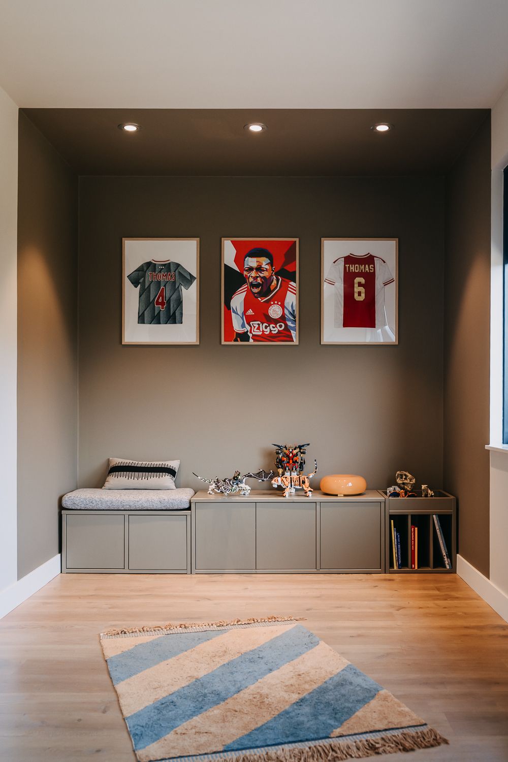 Overzicht van tienerkamer met Woood kast, opgeruimd speelgoed en Lego-opslag. Voetbal helden aan de muur in lijsten.