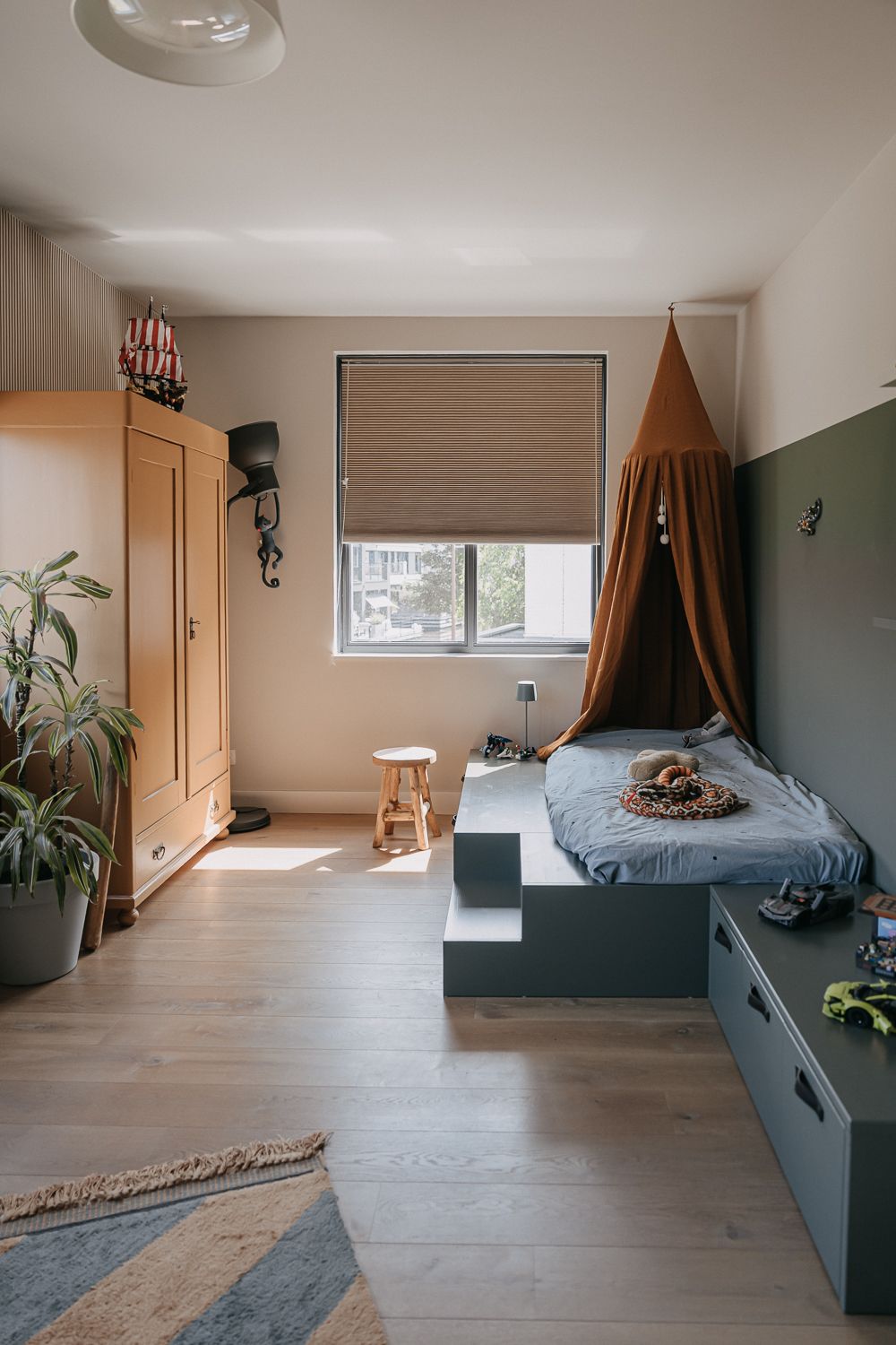 Overzicht van een opgeruimde kinderkamer met authentieke geschilderde kast, Lego-opslag en bed met klamboe. VT wonen bed en kast.
