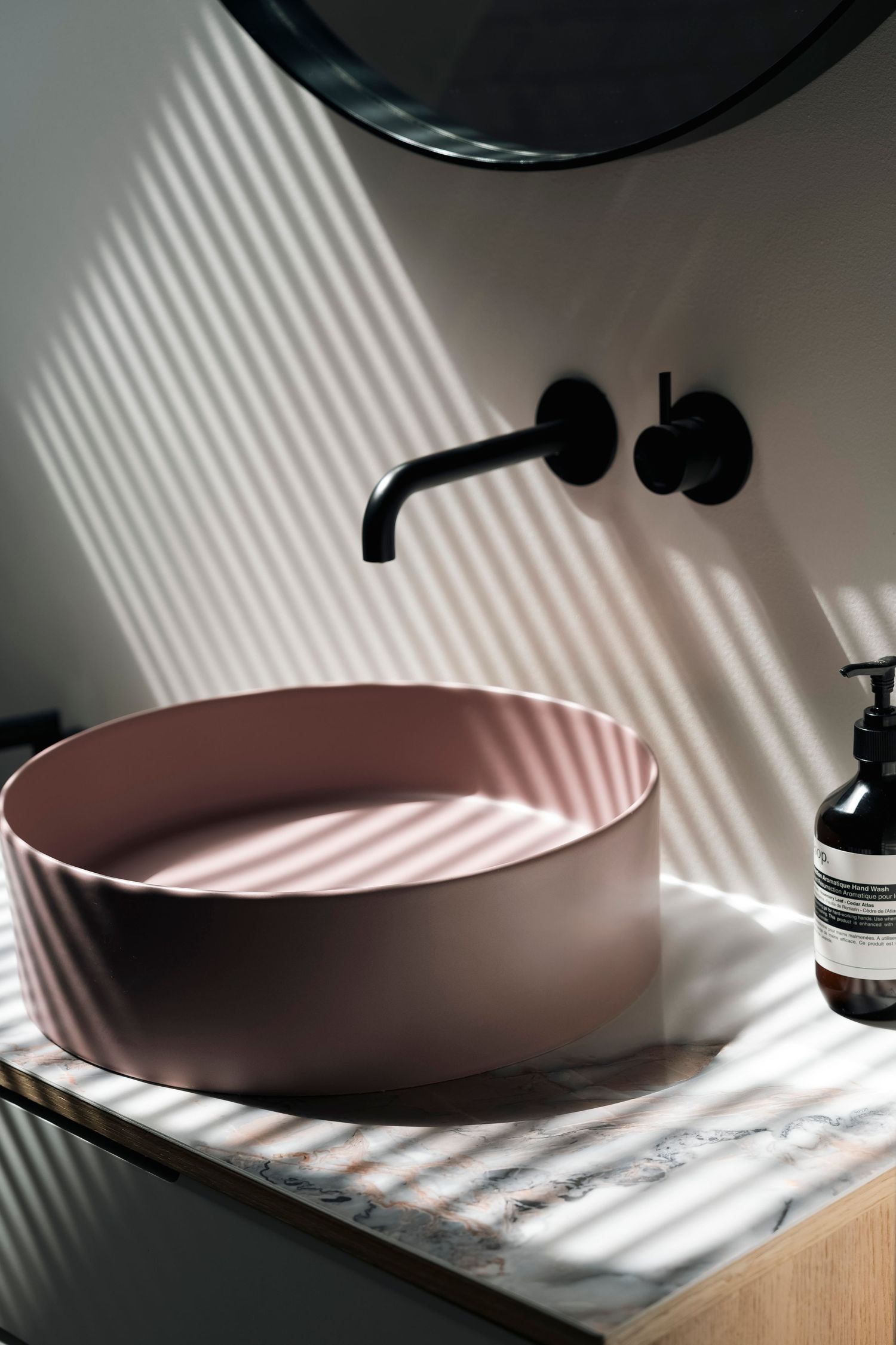 Elegant badkamermeubel met strakke roze wasbak, warme materialen en verfijnde styling van Milk Interieur. Veel reflectie vh raam.