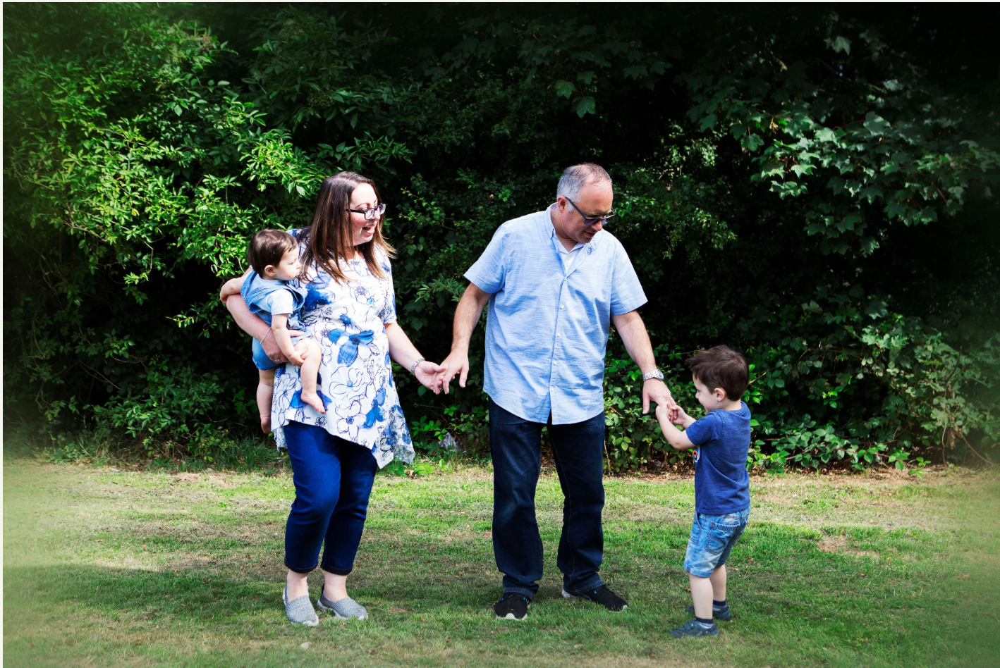 Candid family portrait with parents and two young children in a natural outdoor setting in Prestwich
