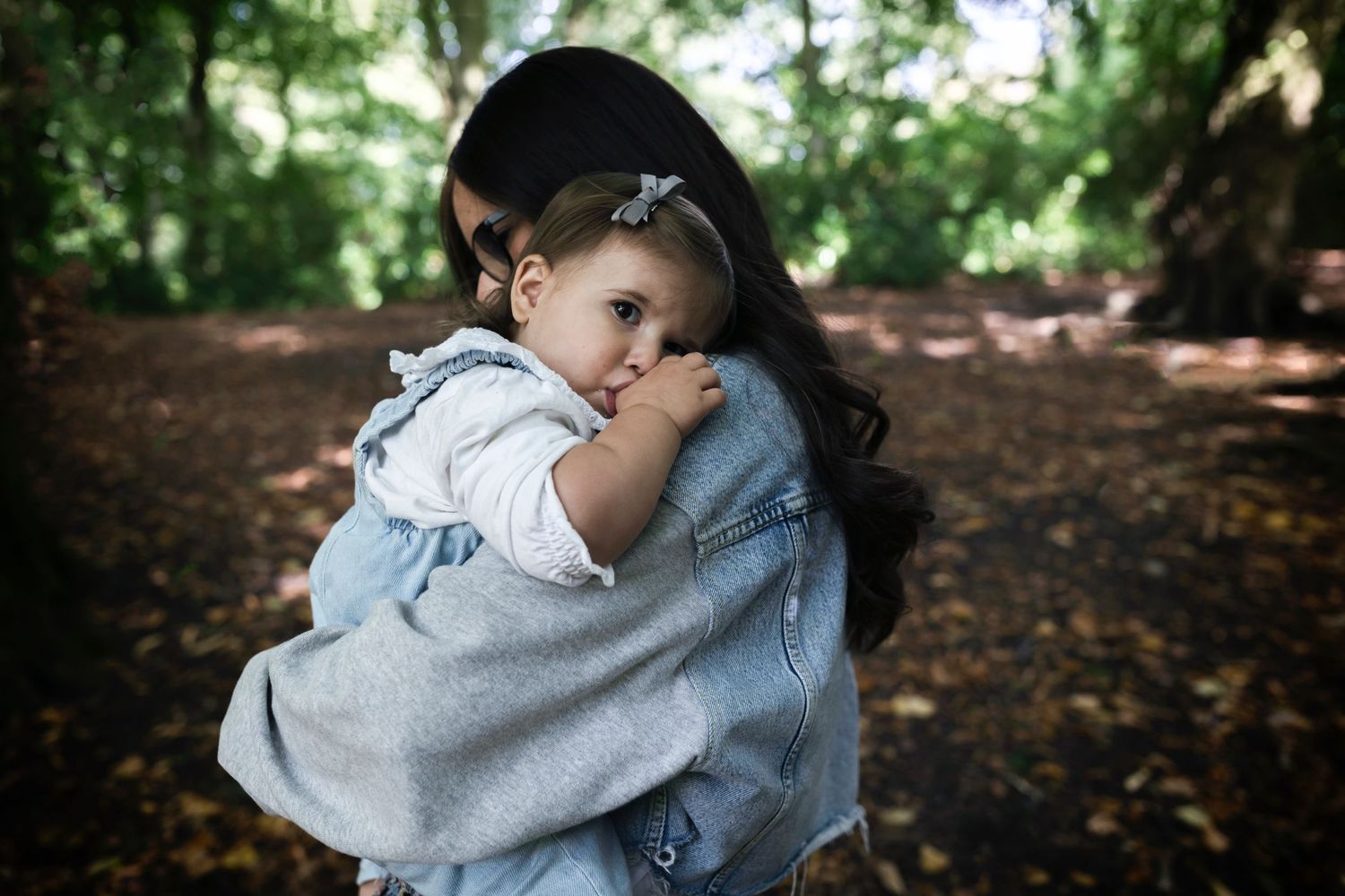 A mother carrying her young, sleepy daughter during a  professional family photo session in a local park in Whitefield, Manchester