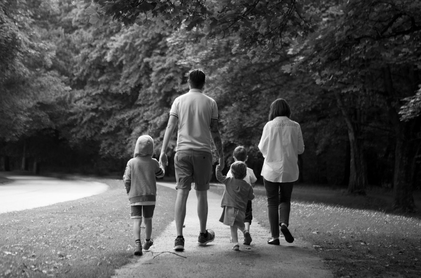 A family of five walking hand-in-hand into a park, enjoying a relaxed and joyful moment together during a family photo session in Prestwich,