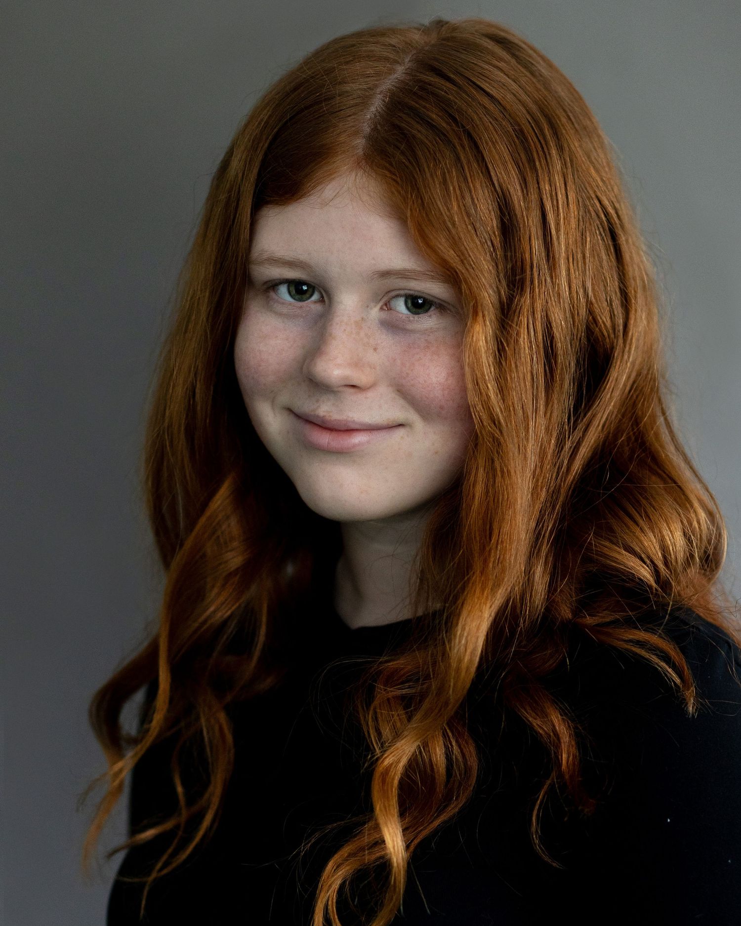 A red-haired girl in Prestwich, captured in an acting headshot, smiling confidently at the camera during a professional headshot session