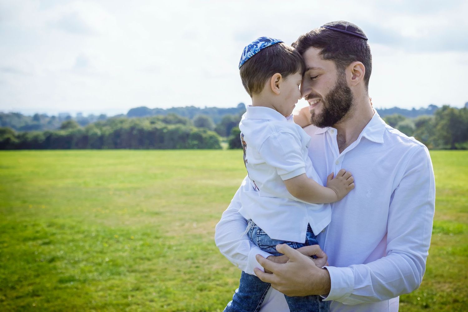 Father holding his son in his arms, both gazing into each other's eyes in a local park in Prestwich, captured during a family photo session