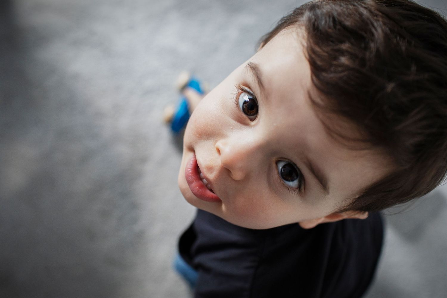 A  candid photograph of a young child's face looking up at the camera in his home in Manchester, UK during a family photo session.