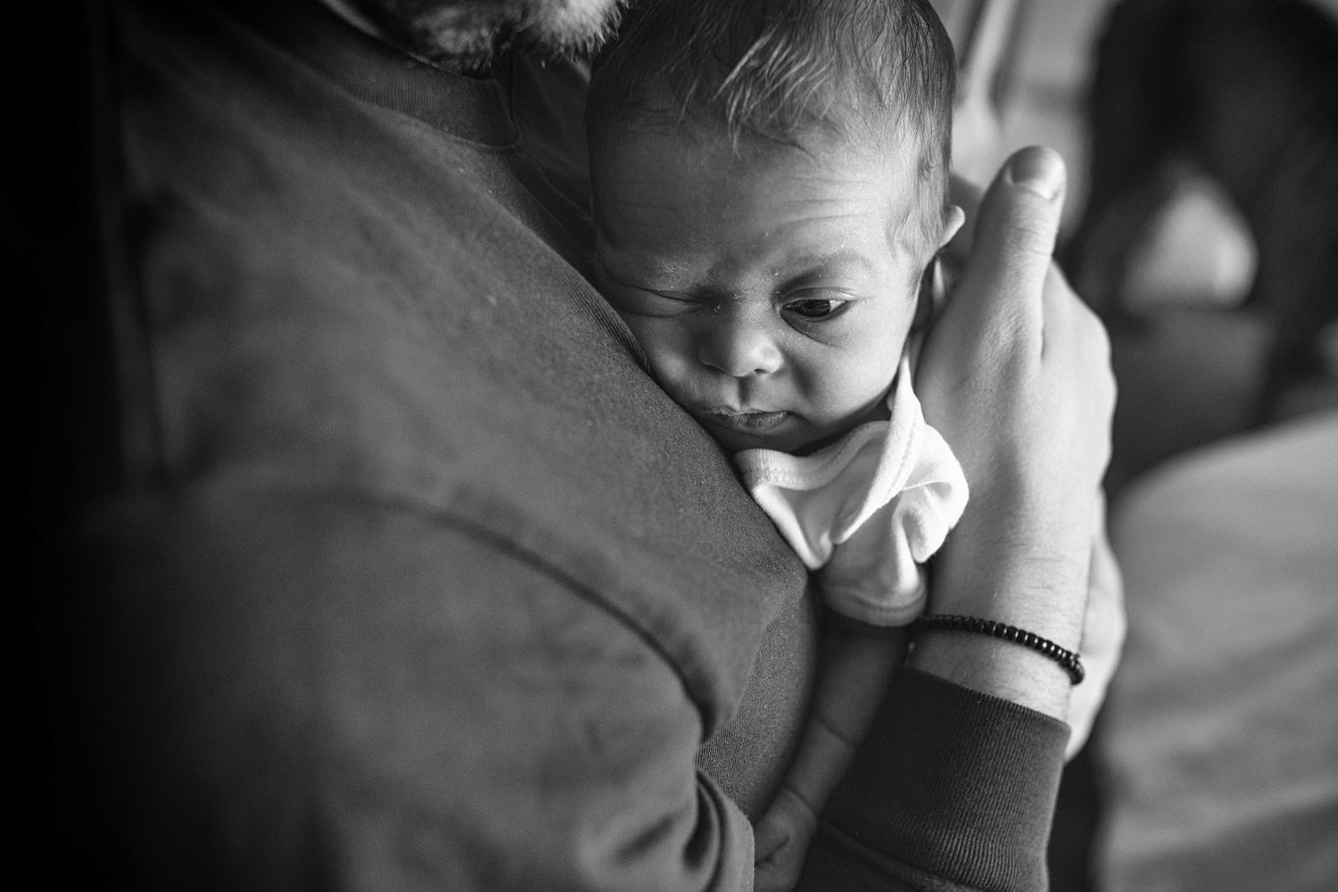 Father gently cradling his newborn in a serene and loving pose, captured in a home setting in Prestwich, Manchester