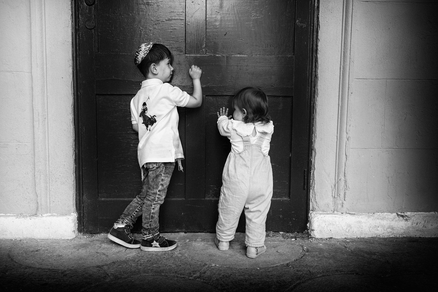 Two siblings playfully knocking on a door in a park, and enjoying their time together during a family photo session in Prestwich, Manchester