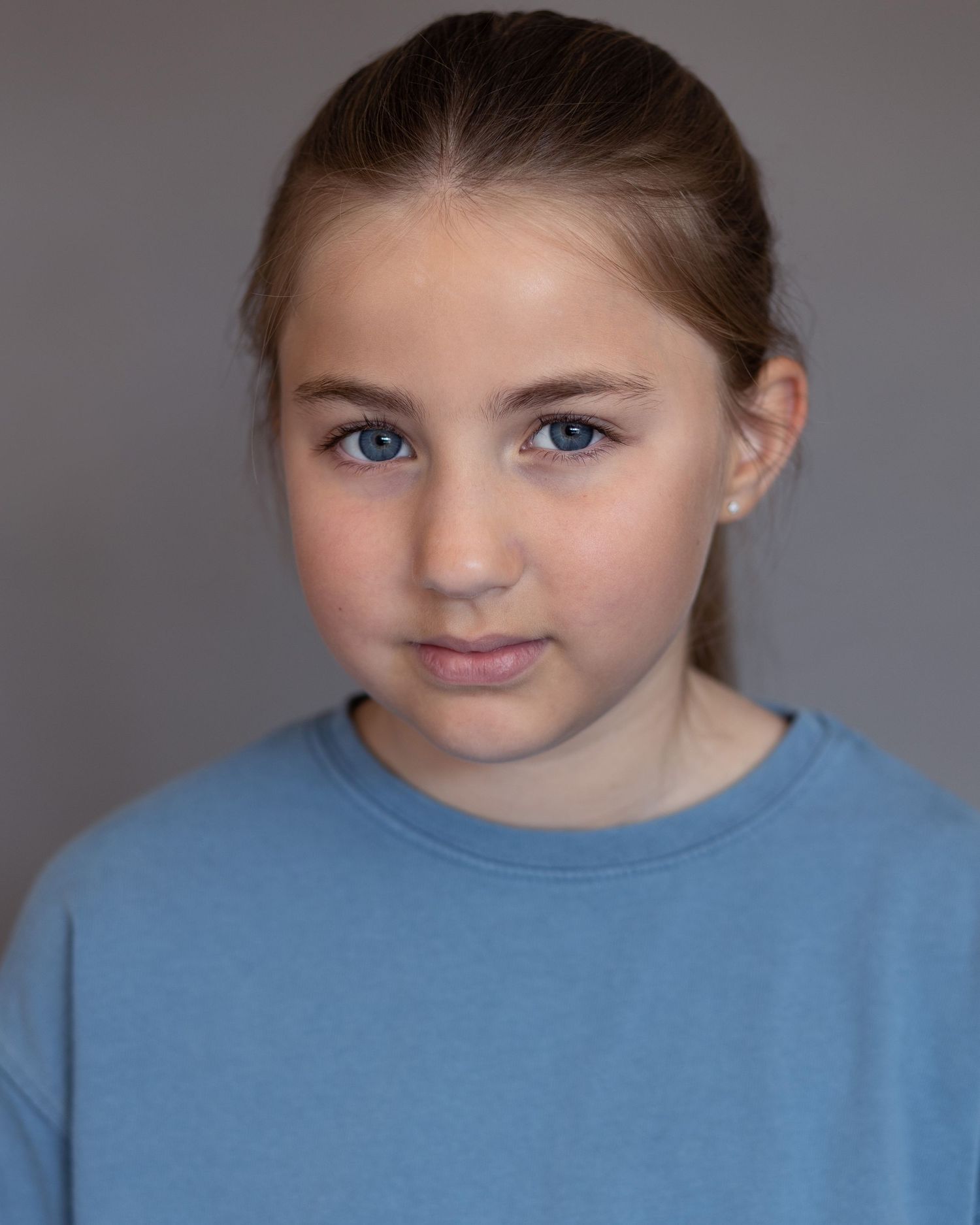 A young girl with her hair in a ponytail posing for an acting headshot in Whitefield, showcasing confidence during a professional session