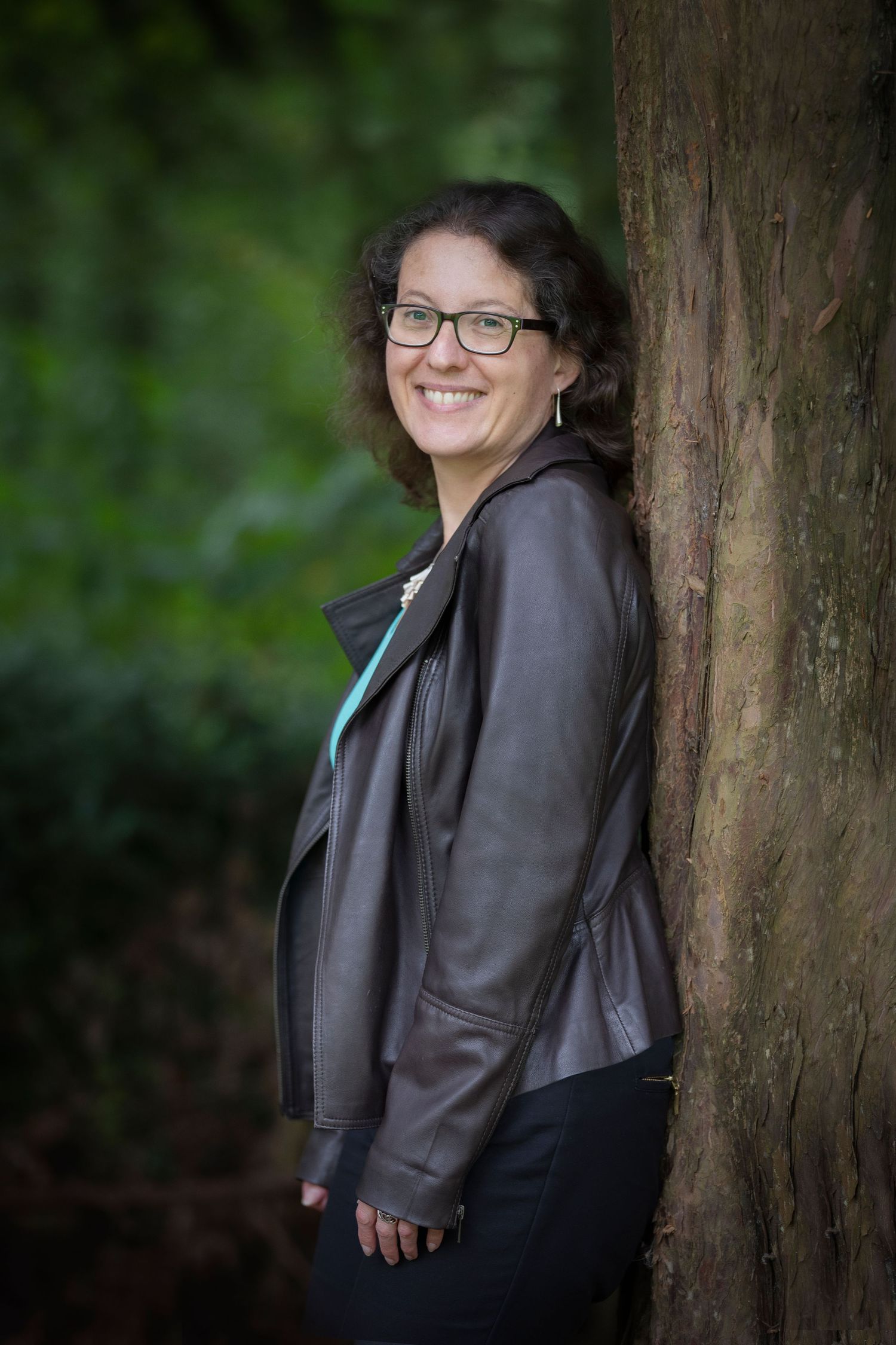 A woman leaning against a tree in a park in Whitefield, Manchester, smiling, happy, and confident during a personal branding session