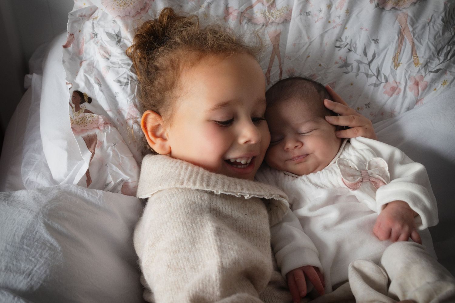 Older child lovingly cuddling her new baby sibling at home in Prestwich, surrounded by warmth and tenderness in this intimate family moment.
