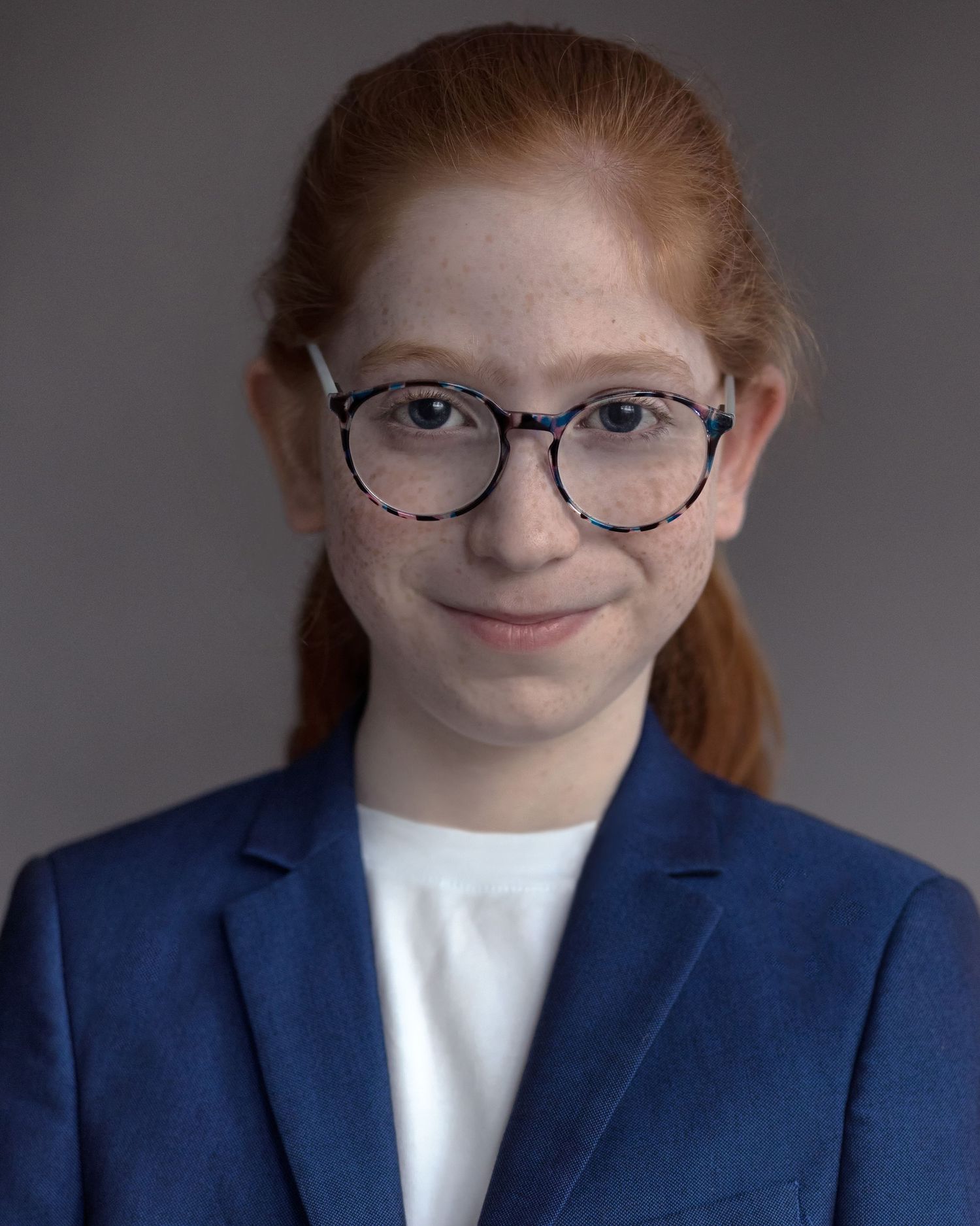 A red-haired boy with long hair and glasses posing for an acting headshot, exuding personality during a professional session in Manchester