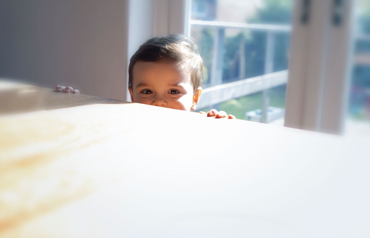 Photograph of a little boy peeking above the kitchen table at his family home in Manchester,  captured during a family photography session