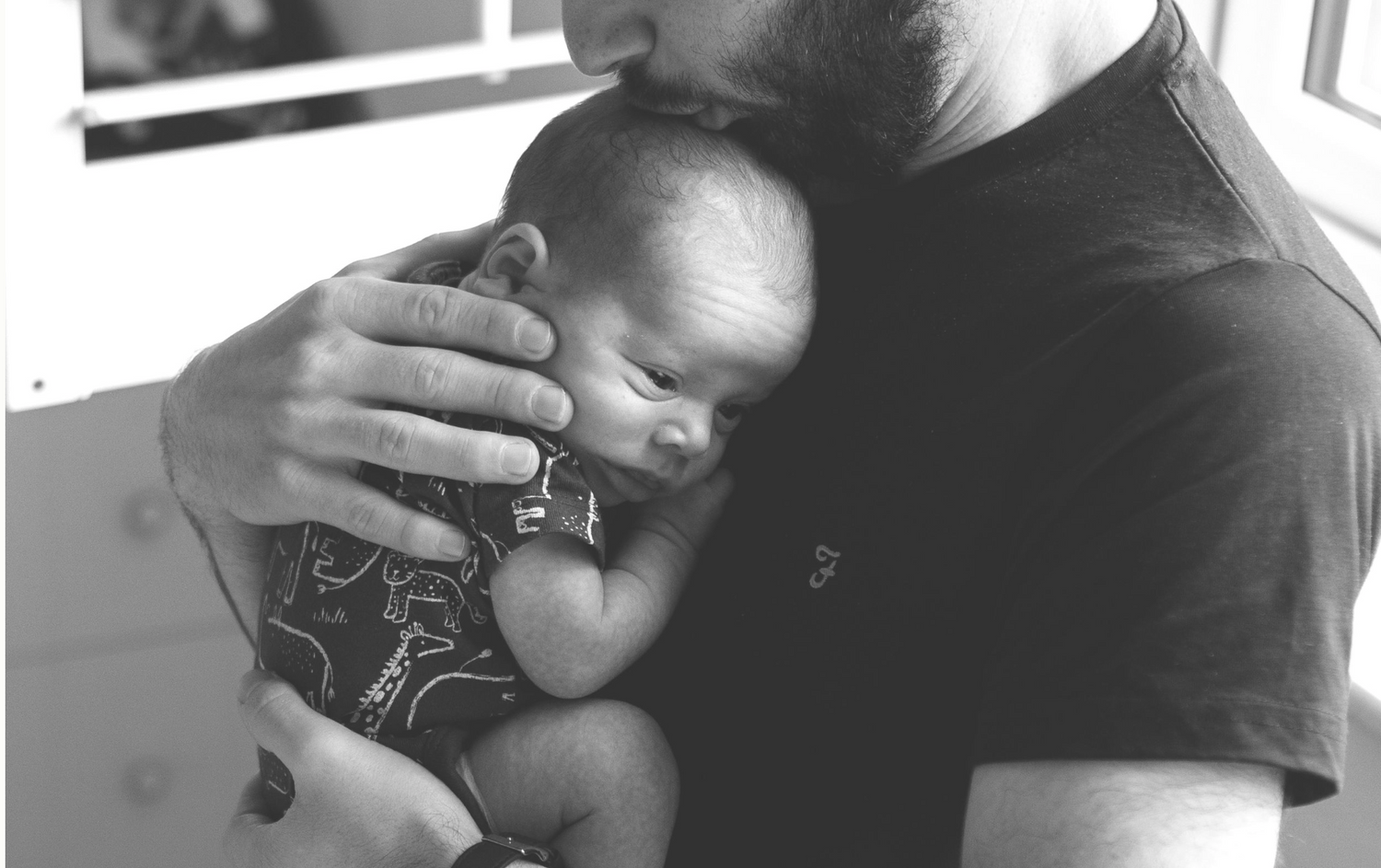 Dad cradling and kissing his newborn baby during a peaceful newborn session in their home in Whitefield, Manchester