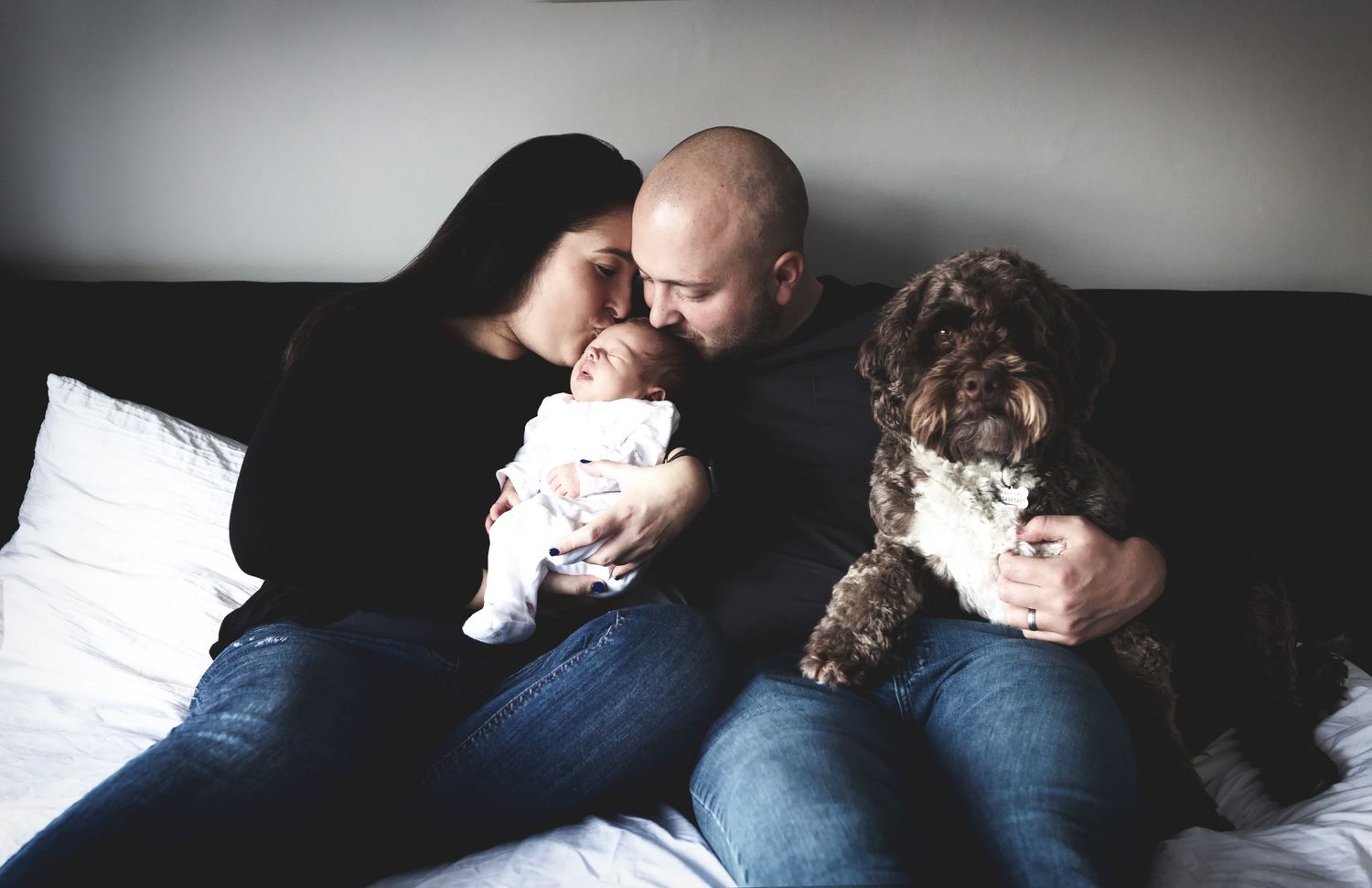 Parents sharing a joyful moment, holding and kissing their newborn baby in the bedroom of their home in Whitefield, Manchester.