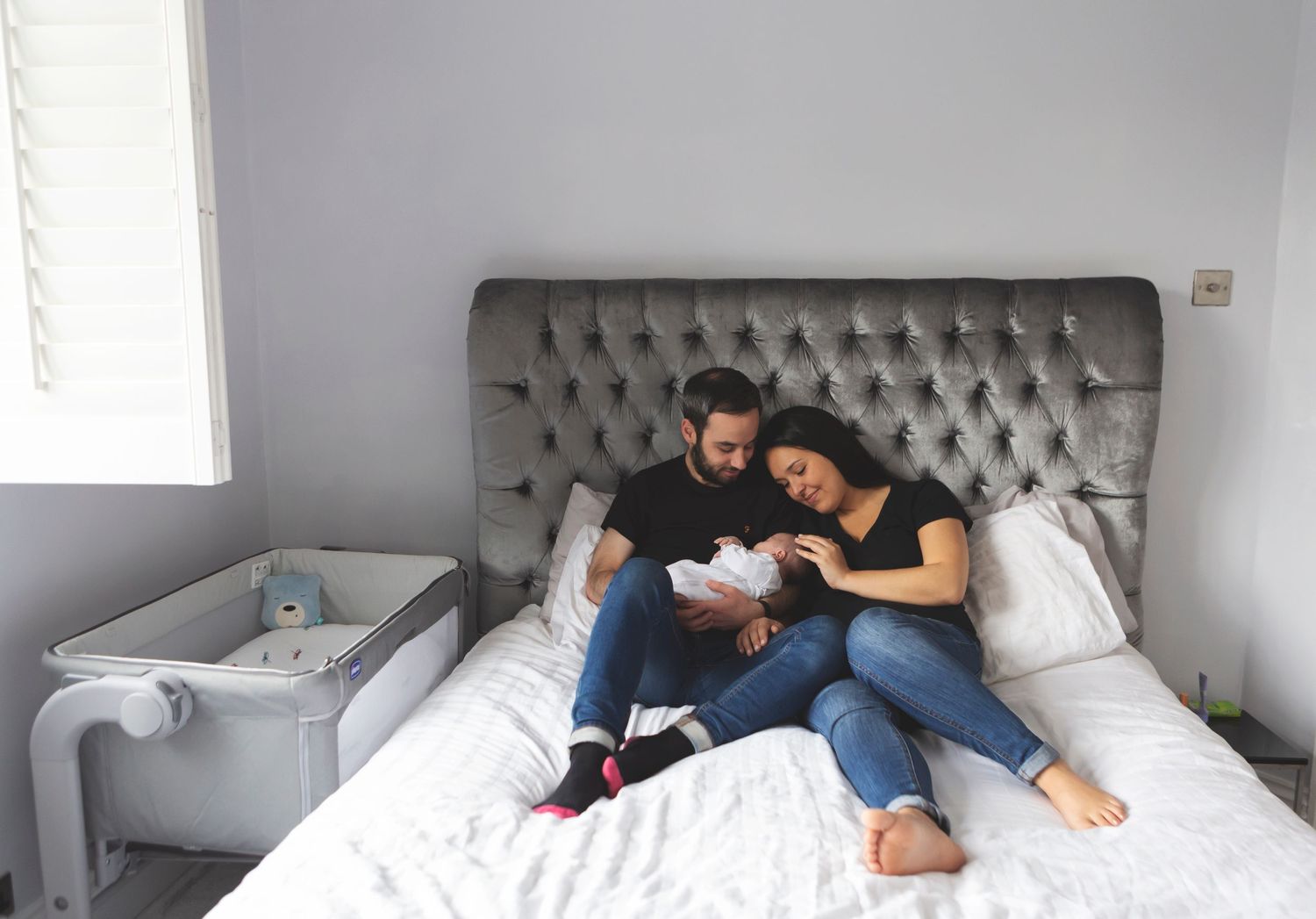 Newborn photography session in Prestwich, capturing a family of three together on the bed. Mum and dad lovingly look at their baby.