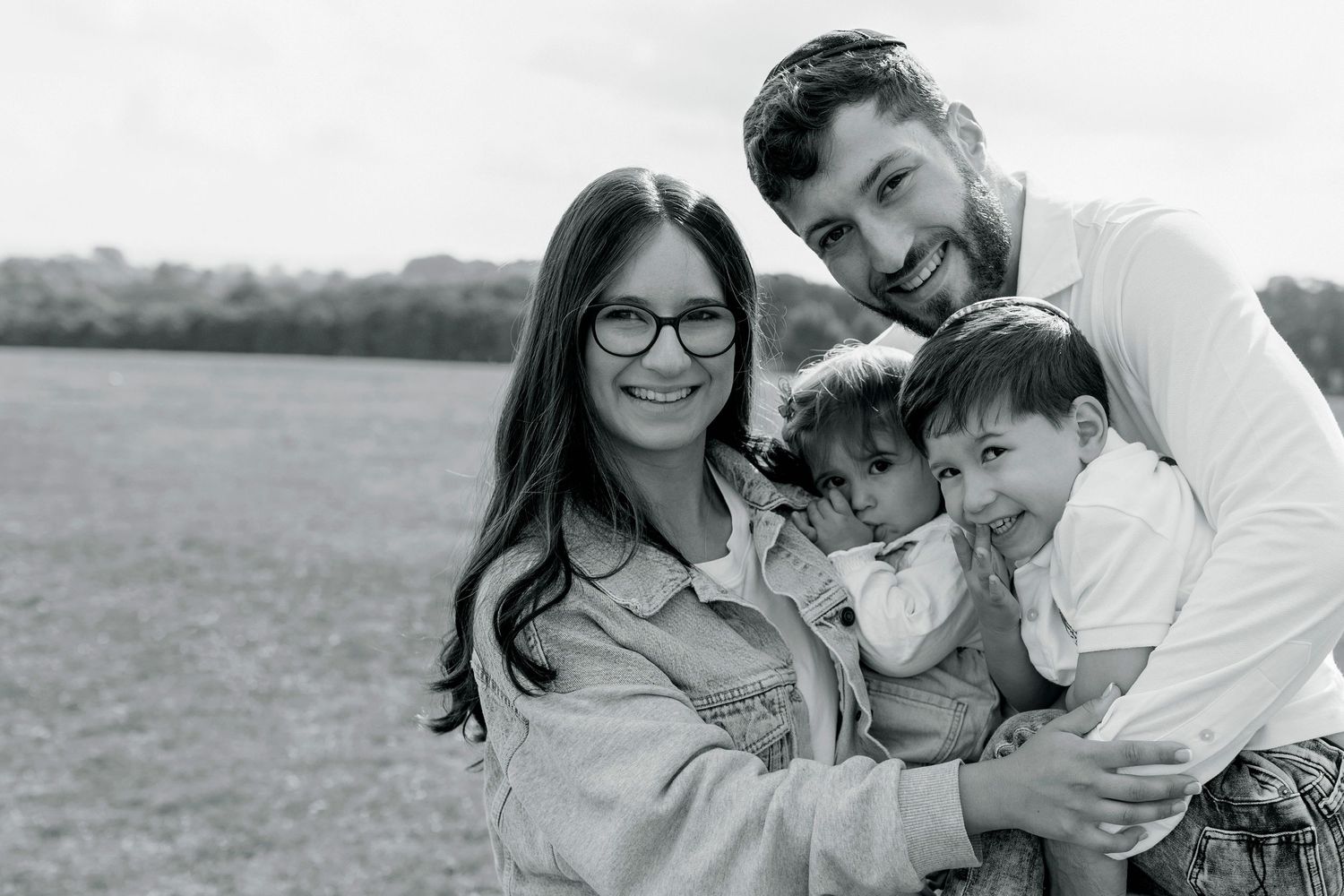 Family of four huddled together, smiling warmly at the camera, enjoying a close and joyful moment during a family photo session in Prestwich
