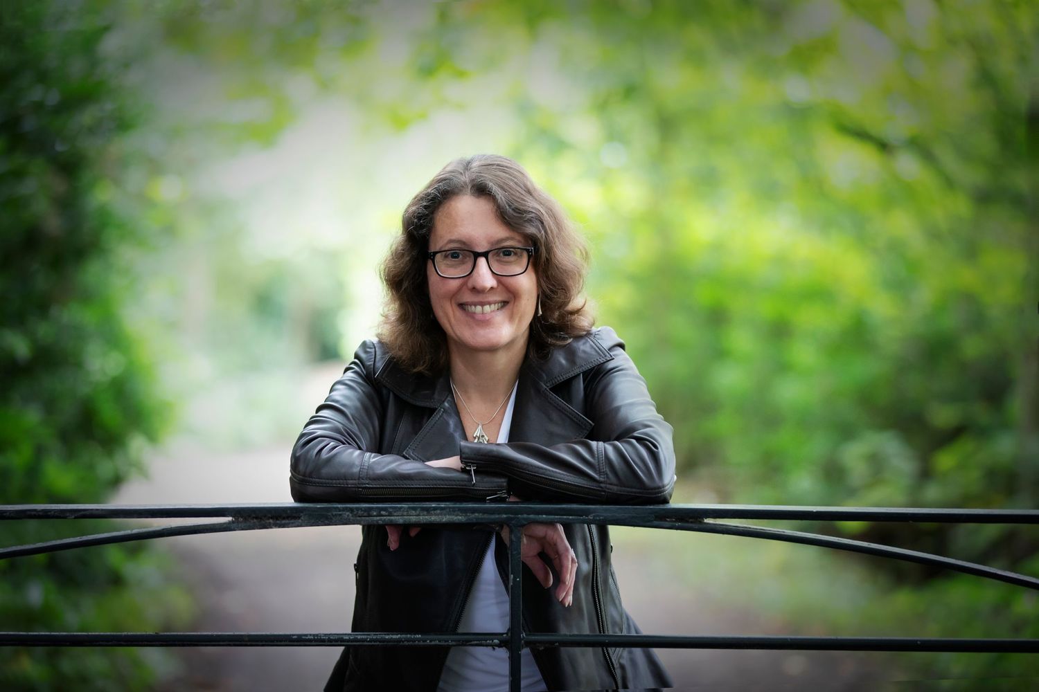 A woman smiling while leaning on a gate in a park in Whitefield, captured during a personal branding session with a confident, relaxed pose